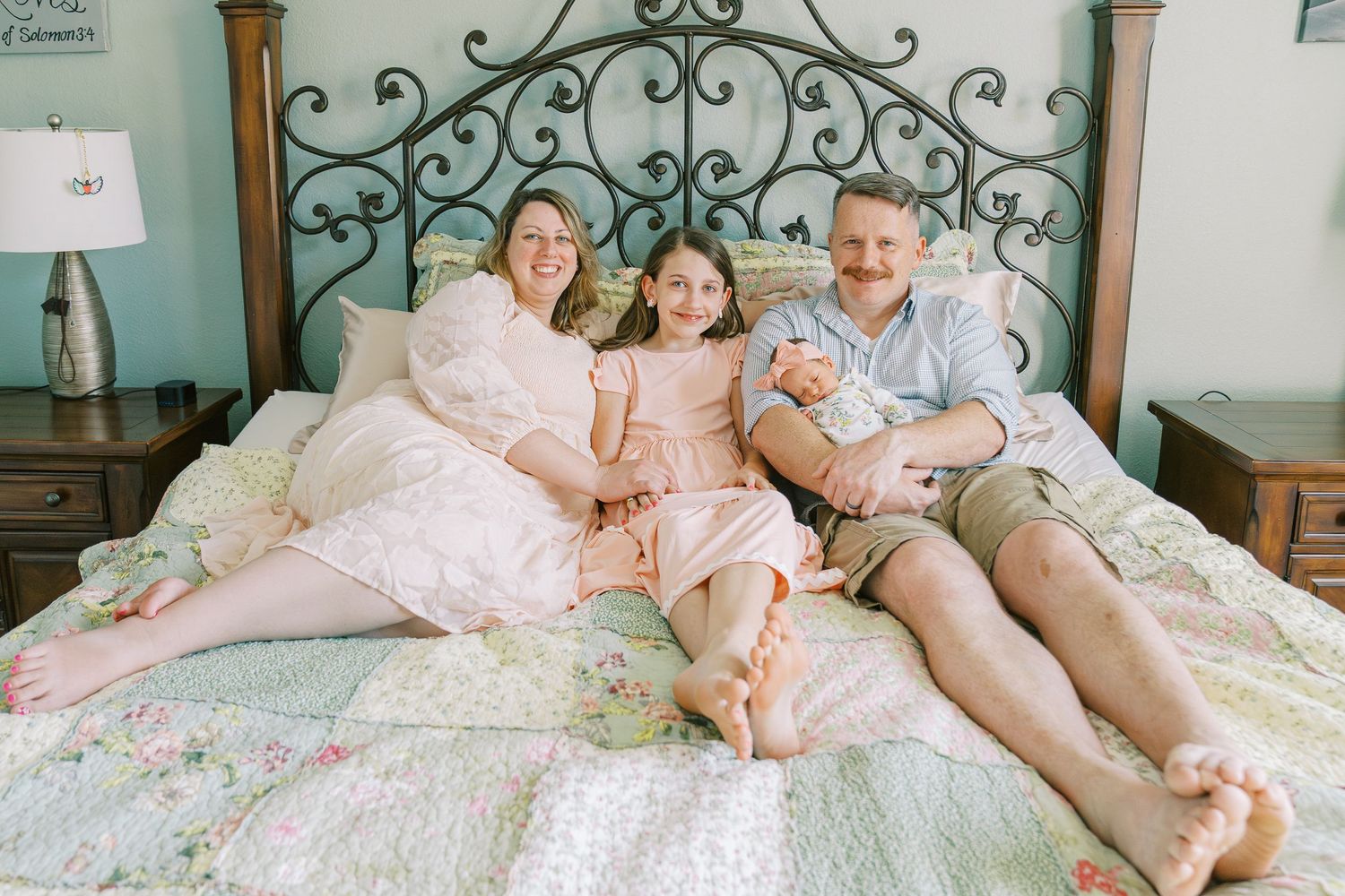 Family relaxing together on ornate bed with floral bedding in cozy bedroom setting.