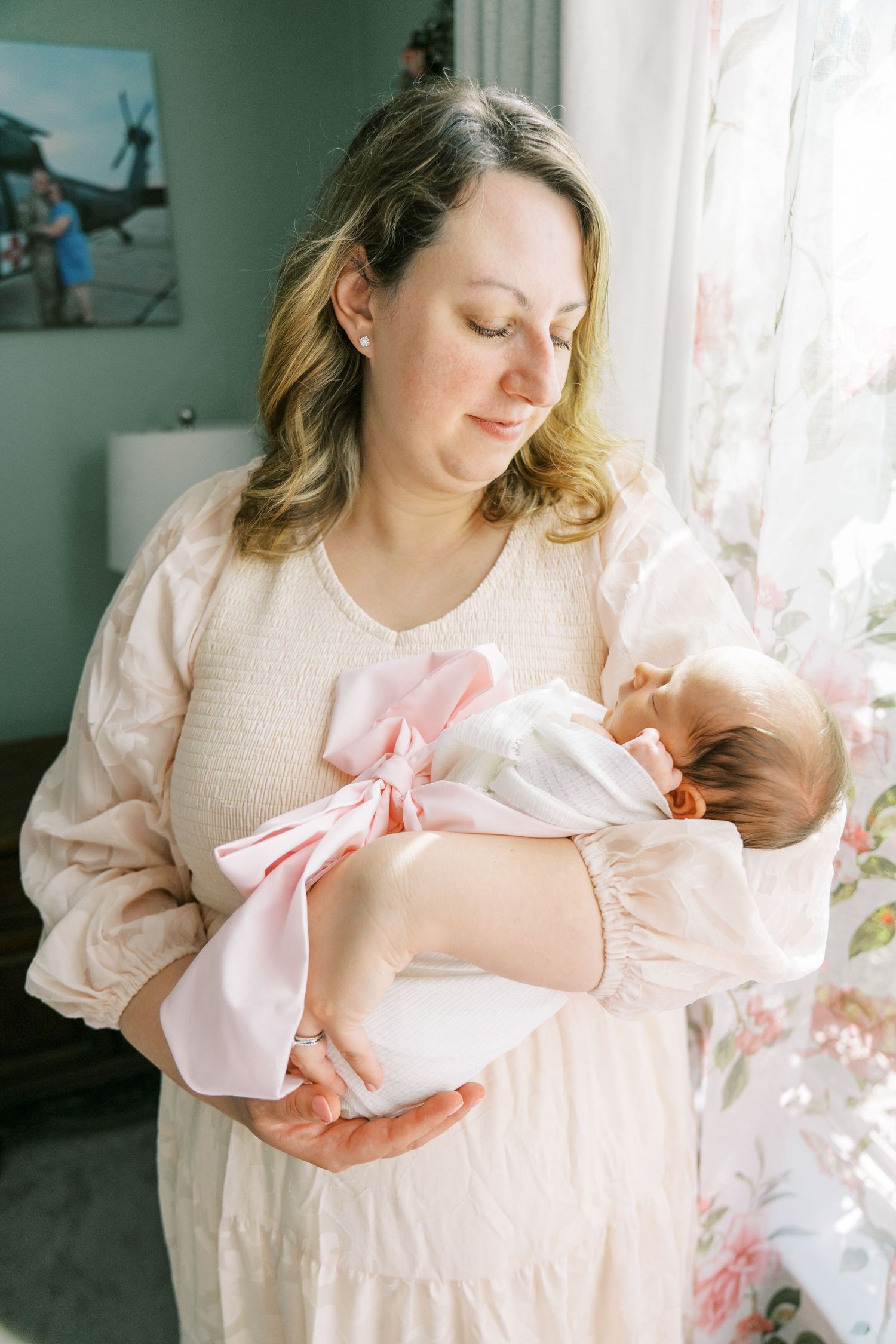 Gentle nursery scene with soft natural light as parent cradles sleeping newborn wrapped in pink bow.