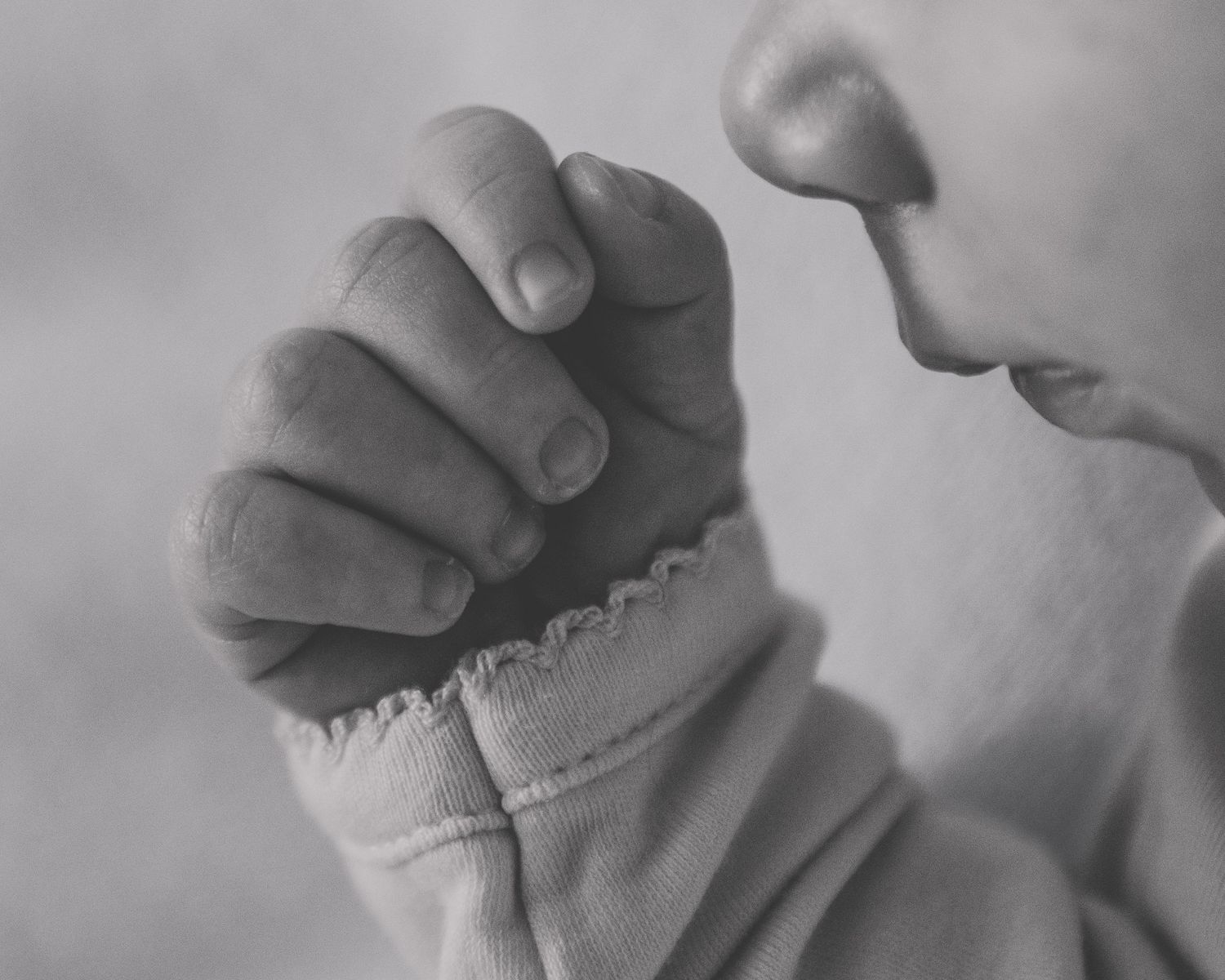 Close-up black and white photo of a sleeping newborn baby's tiny fist near their face.