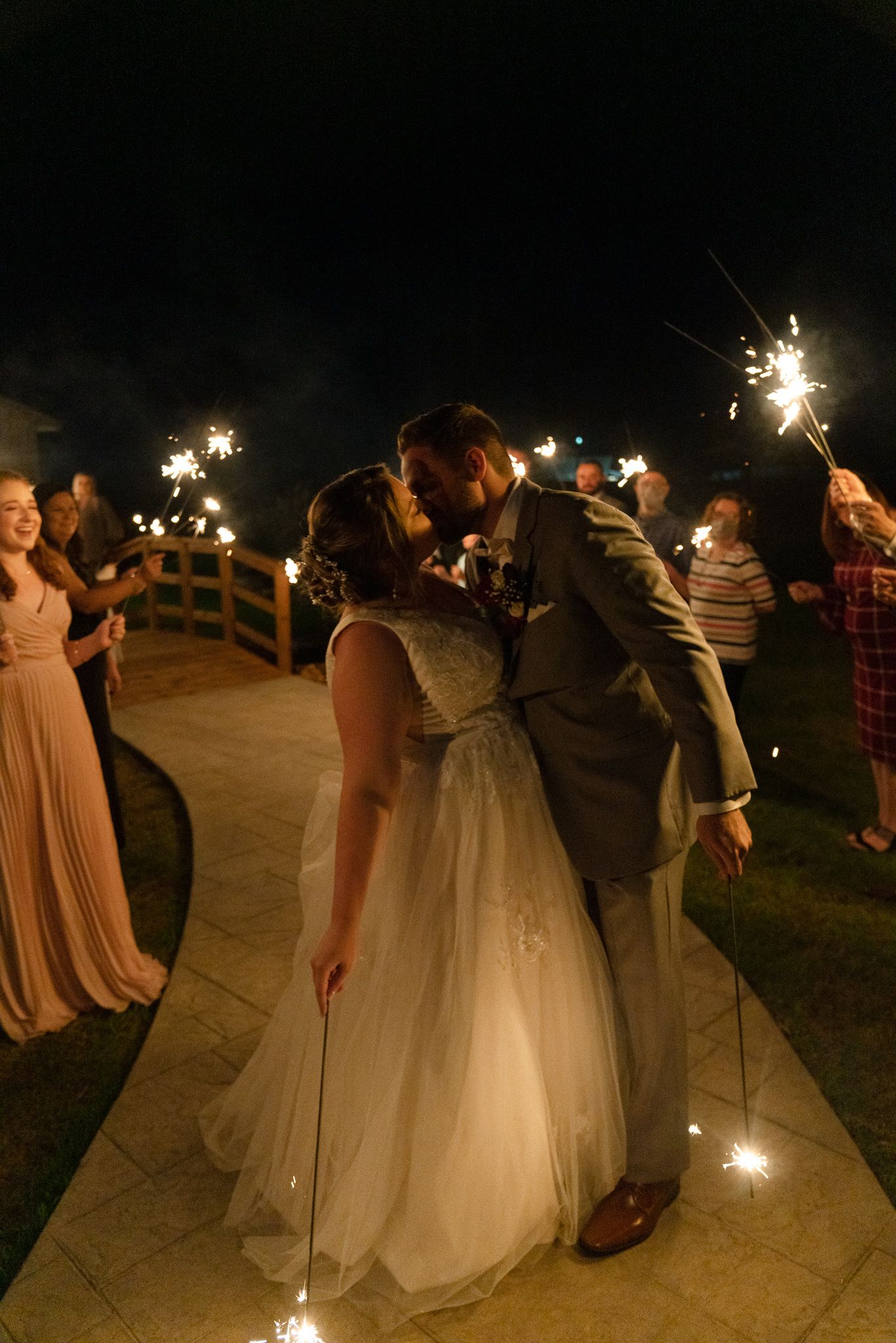 Wedding party celebrates at night with sparklers creating a magical glow along a path during outdoor reception.