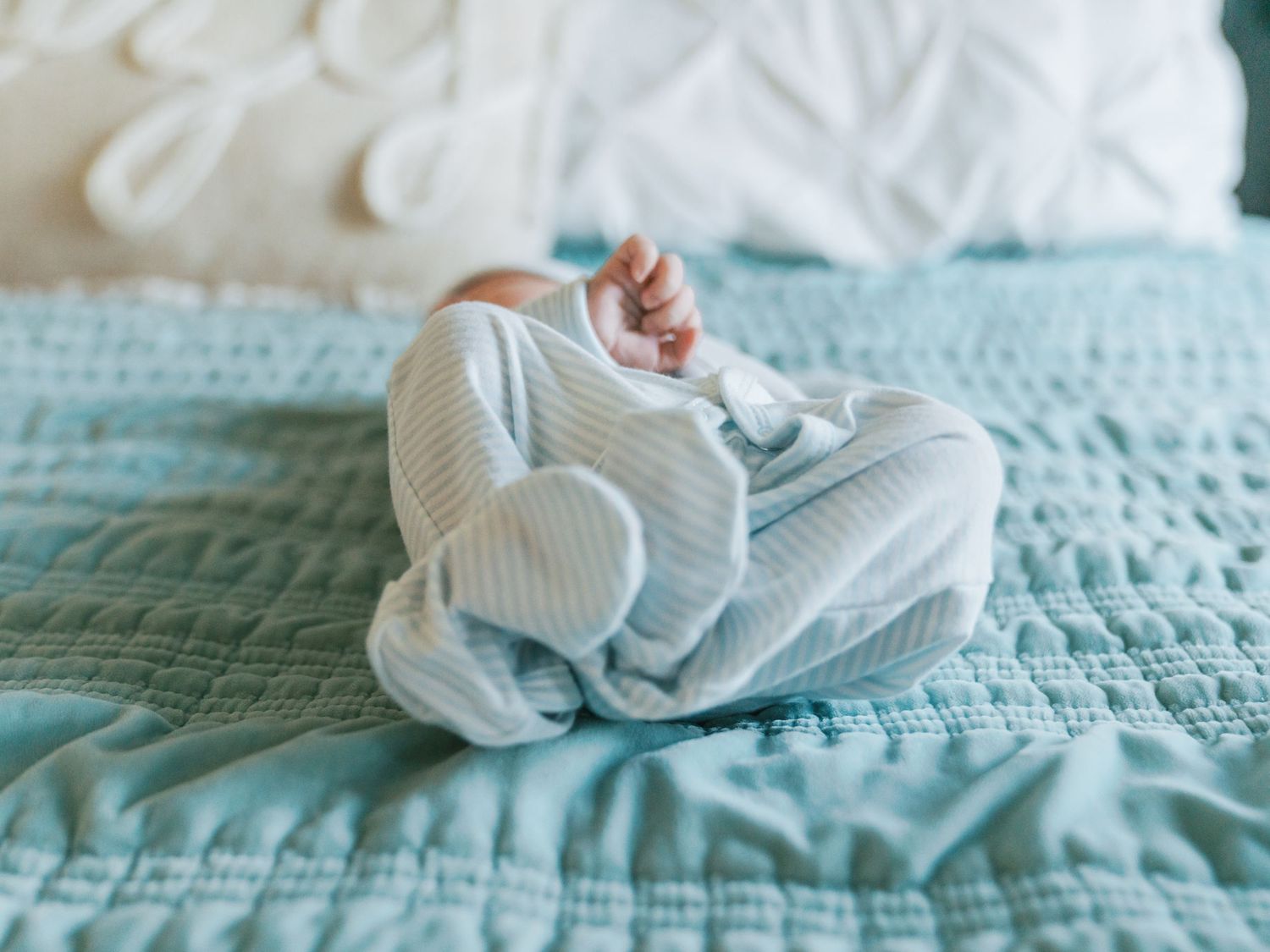 Baby wearing soft white sleepwear rests on a cozy mint green knitted blanket.