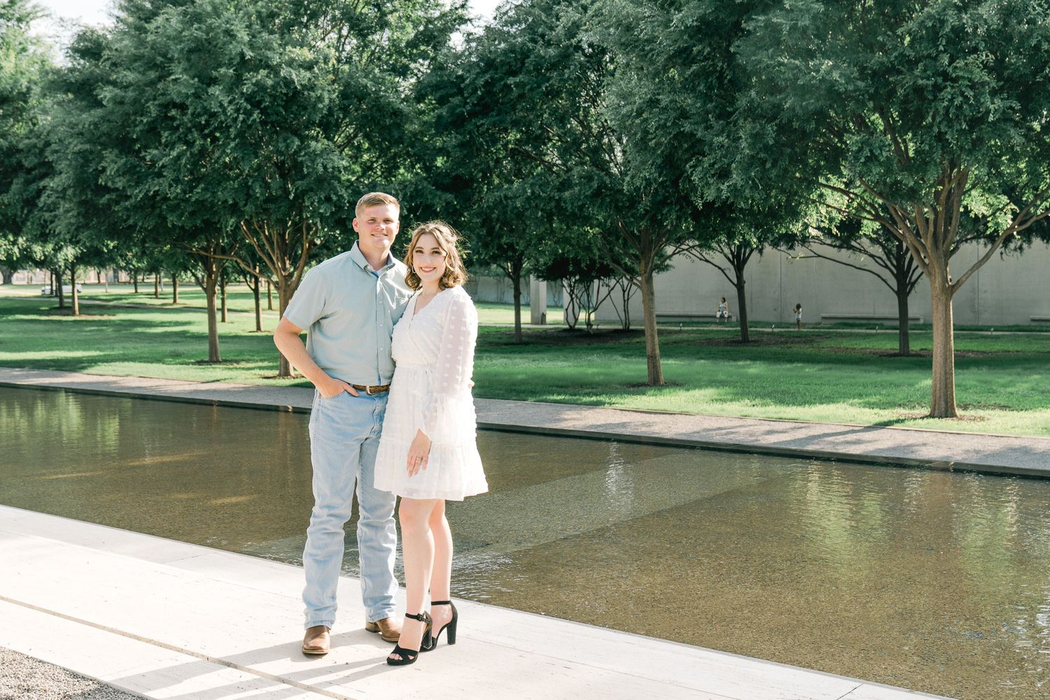 A couple walks hand in hand through a lush green park on a summer day.