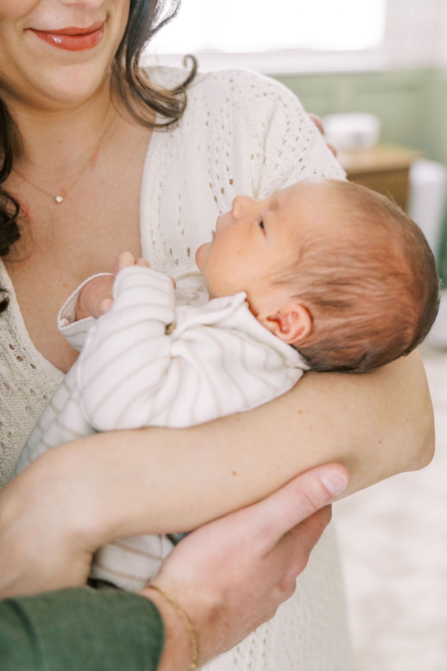 A tender moment between parent and infant wearing white as they embrace in a soft, natural light setting.
