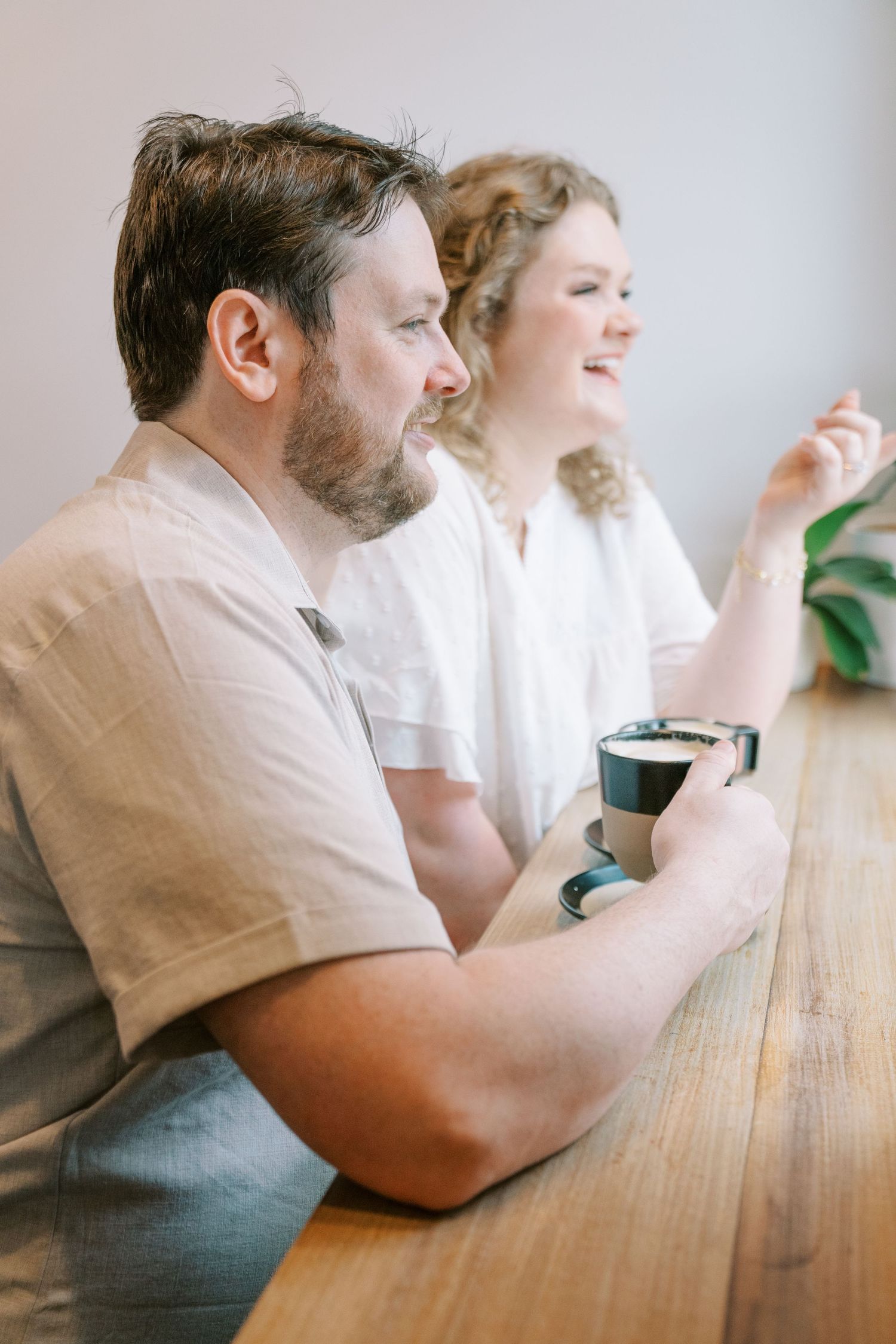 Couple sitting at wooden counter in cafe, man holding coffee cup while woman gestures and smiles.