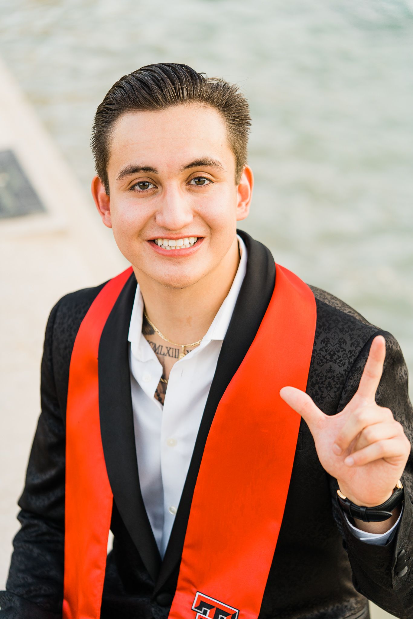 Graduate wearing black suit and red stole smiles and makes peace signs in a series of celebratory graduation photos.