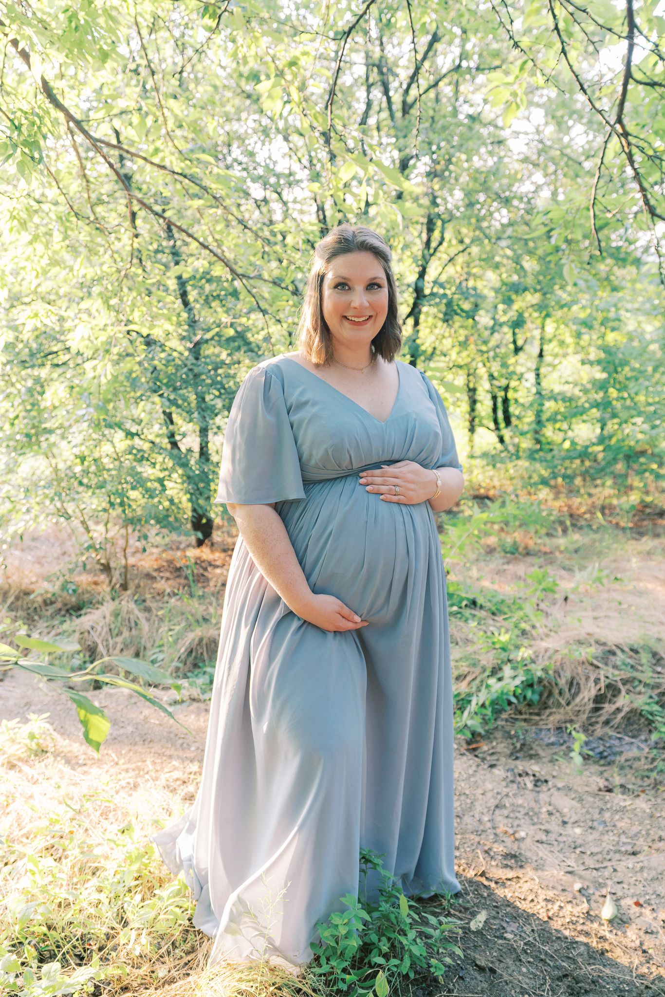 Maternity photo session in a natural outdoor setting with soft lighting and greenery in the background.