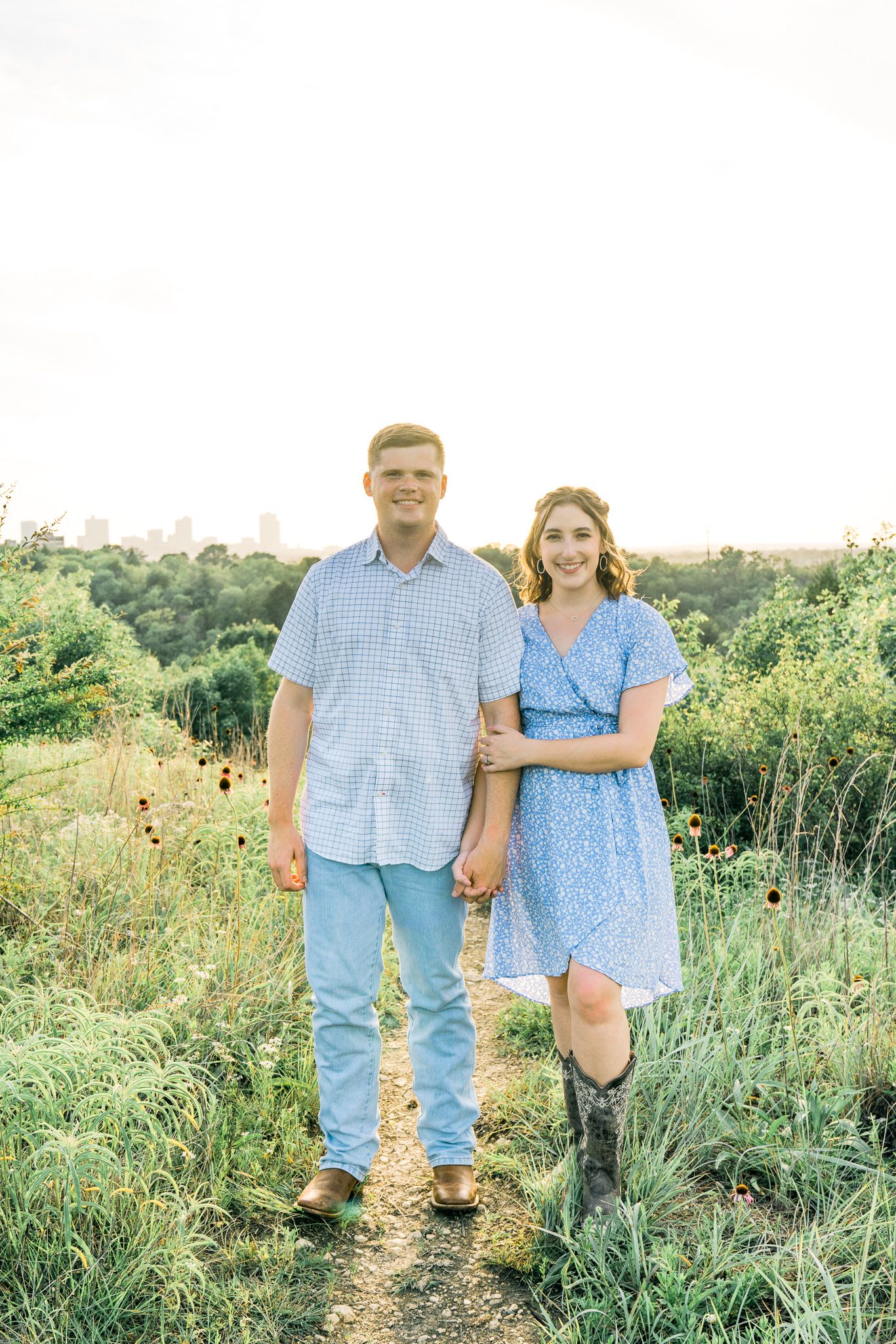 A couple walks together through a scenic meadow on a summer evening wearing coordinating blue outfits.