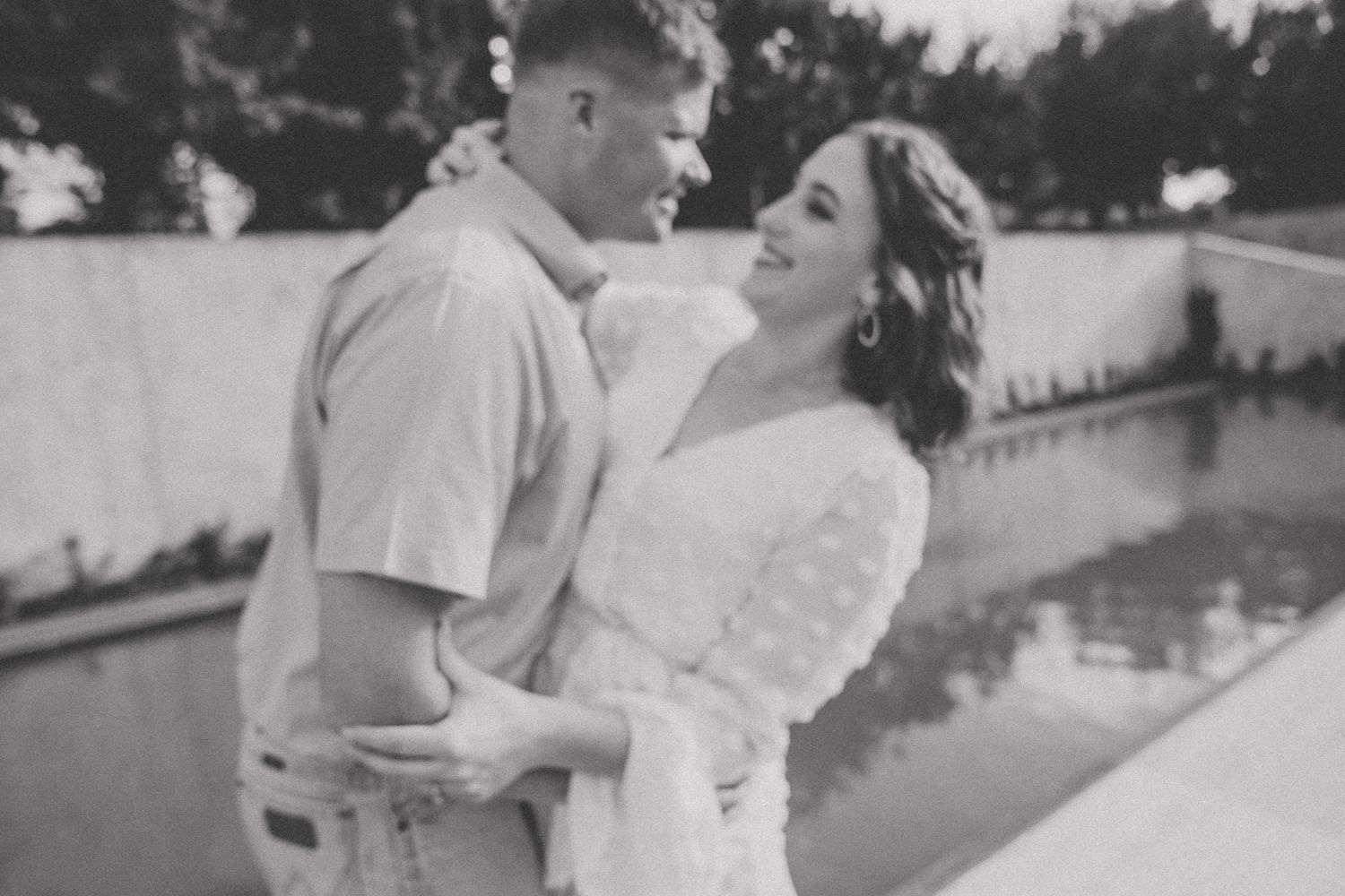 A black and white photo capturing a joyful romantic moment outdoors.