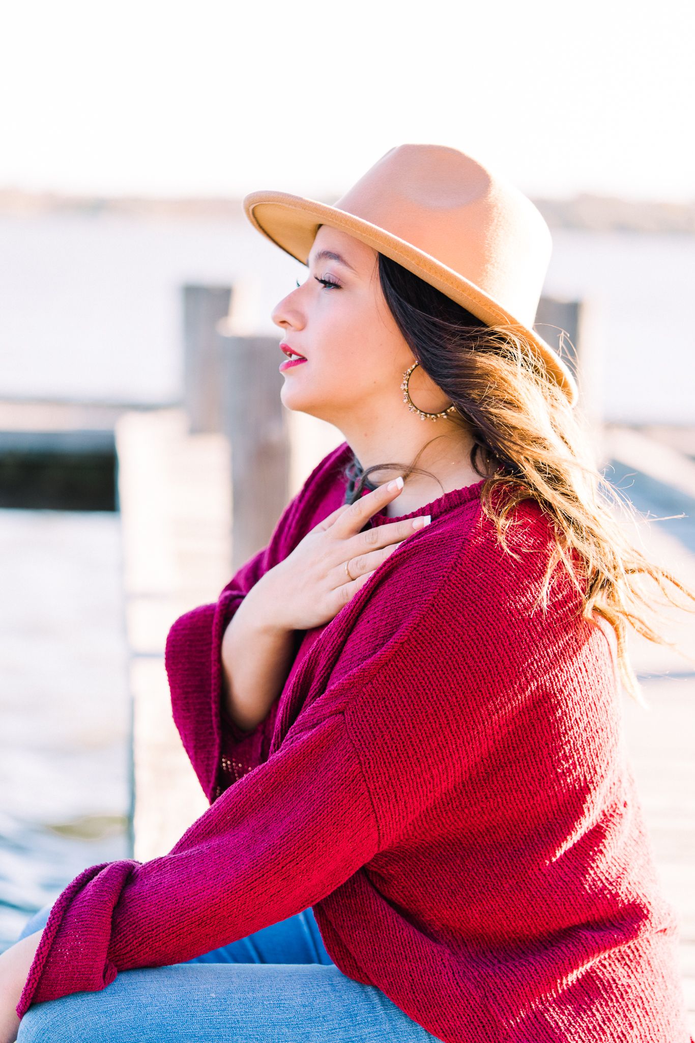 Person in a vibrant red sweater and tan hat poses outdoors against a bright blue sky on a sunny day.
