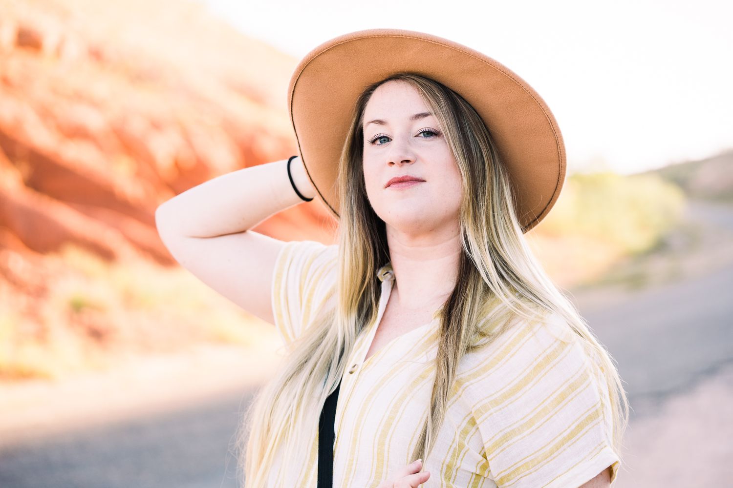 A woman in a wide-brimmed hat poses against a desert backdrop during golden hour.