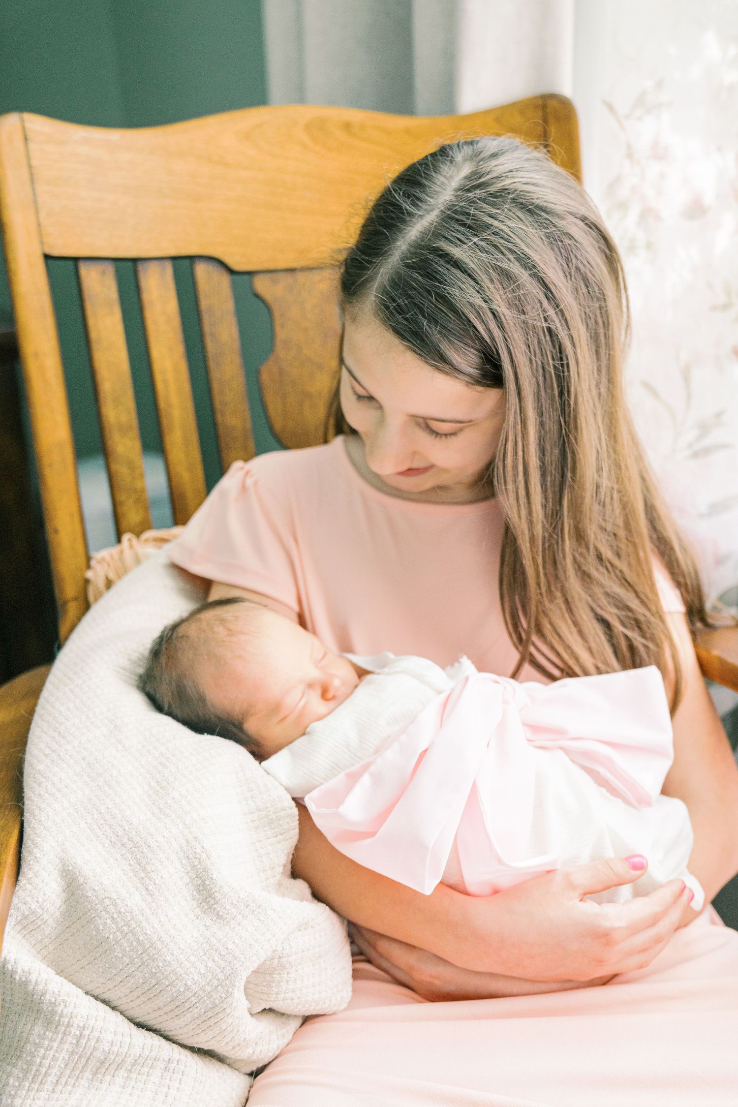 Intimate family portrait in natural light with wooden chairs and white curtains.