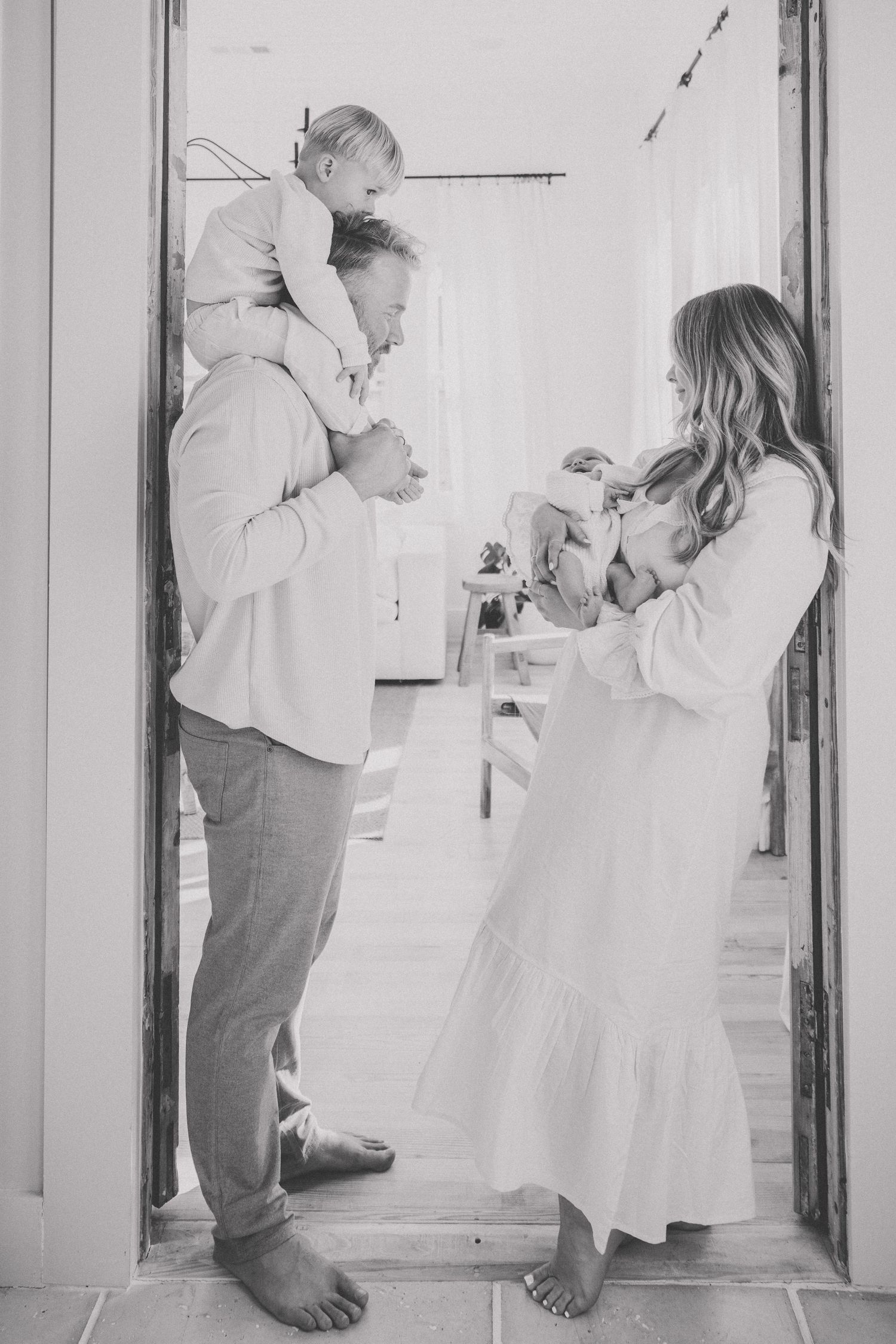 Black and white photo of family sharing tender moment in doorway of home.