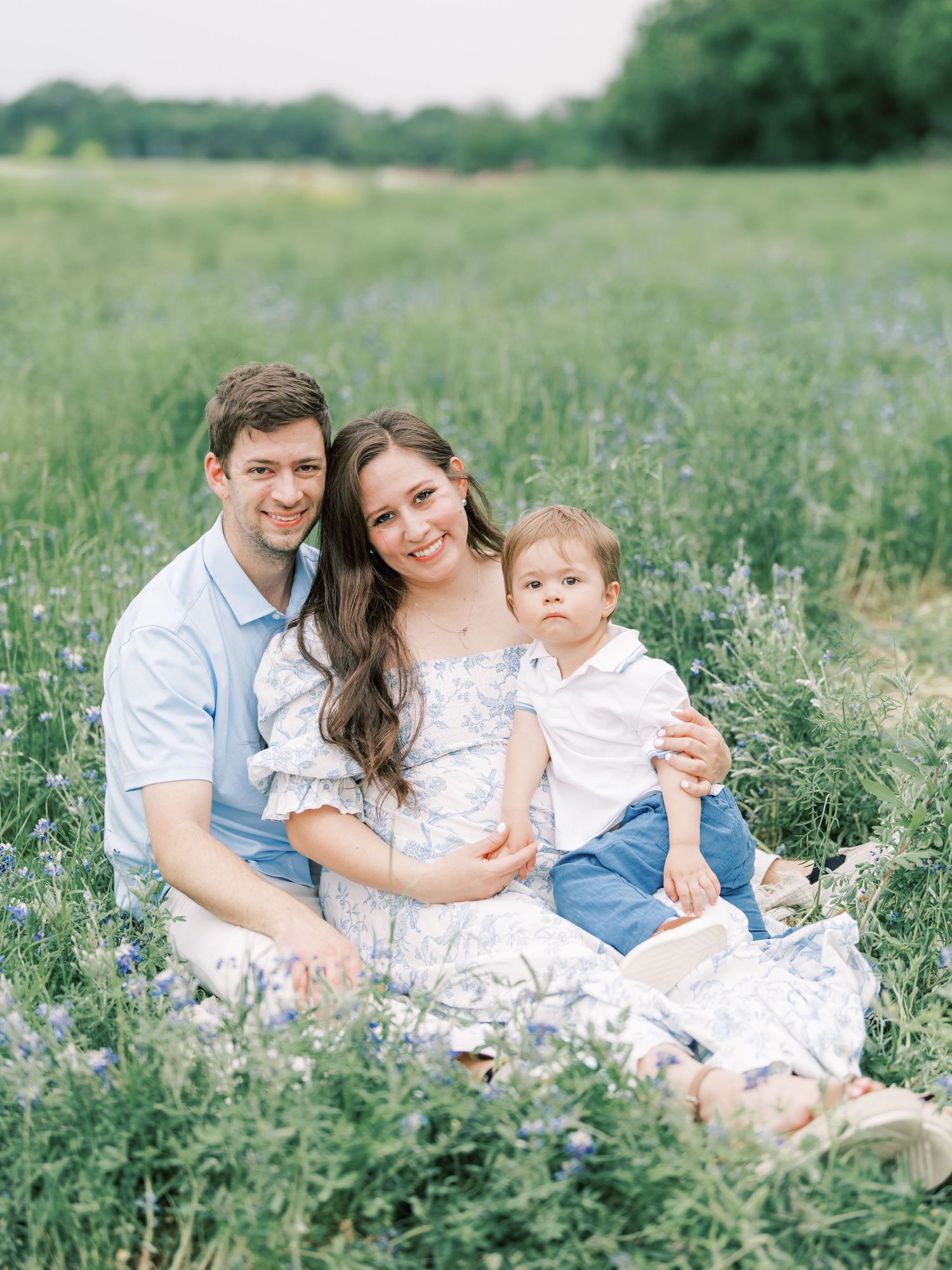 A family sits together in a blooming wildflower meadow wearing coordinated white and blue outfits during a summer photo session.