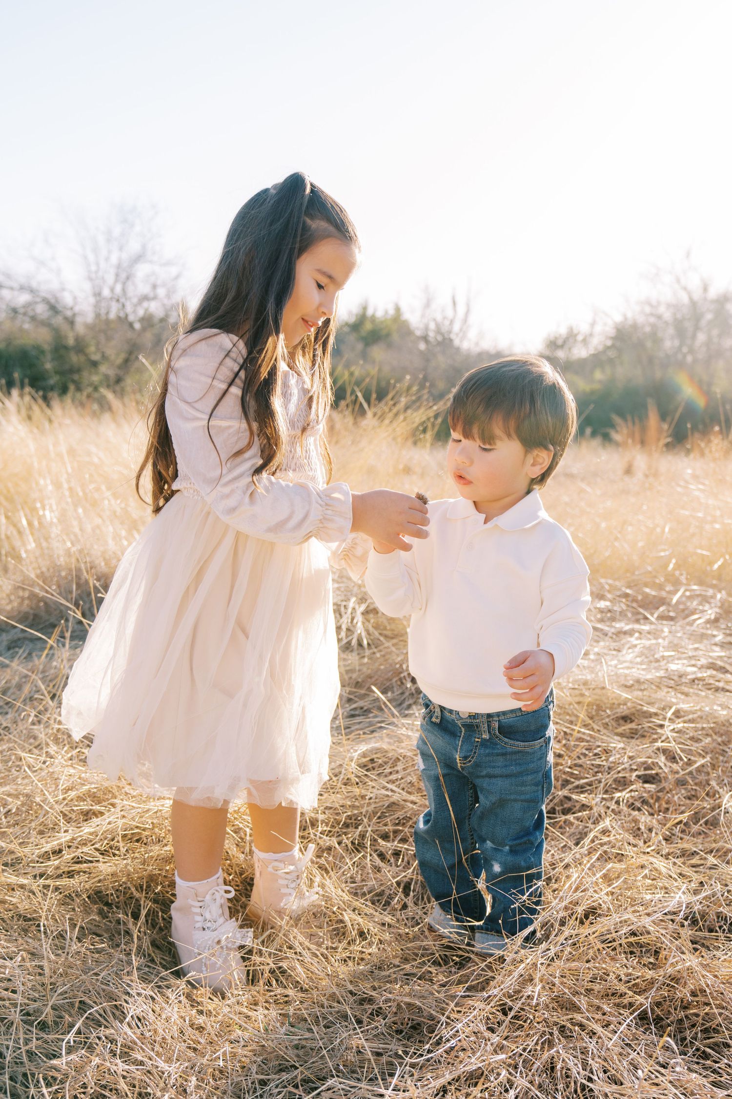A playful moment captured in a golden field with white dress and denim jeans against the setting sun.