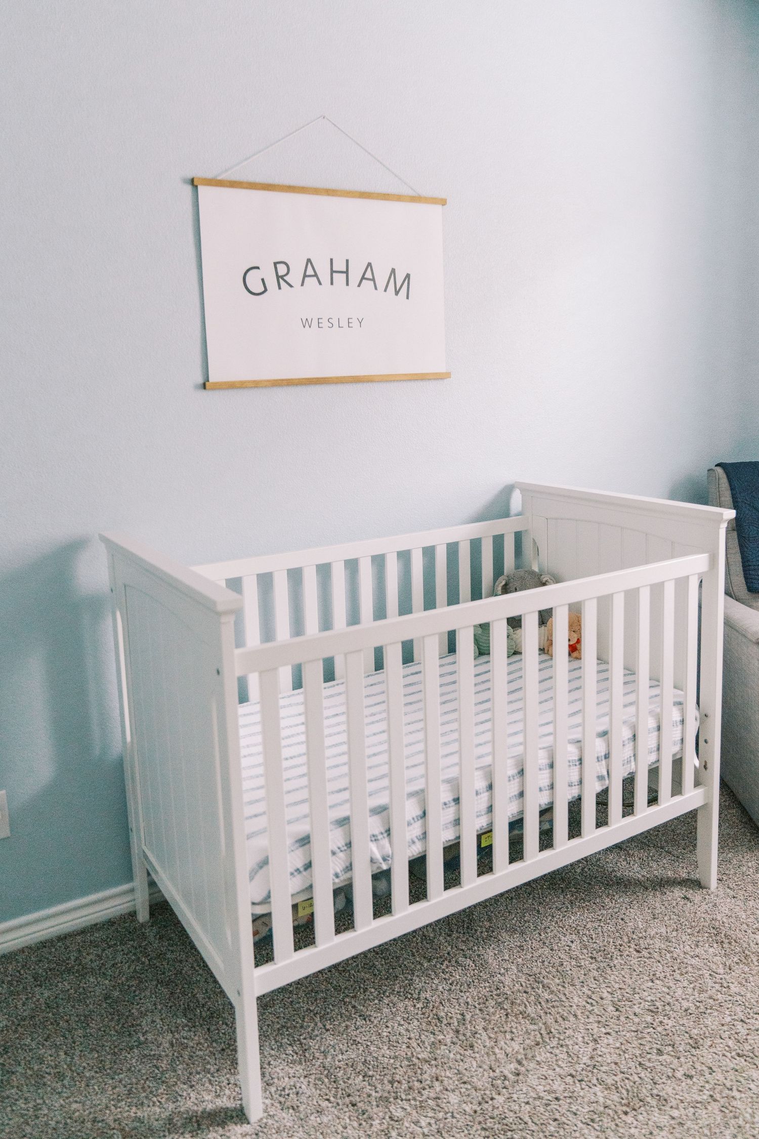 White wooden crib against a light gray wall with a name sign displayed above.