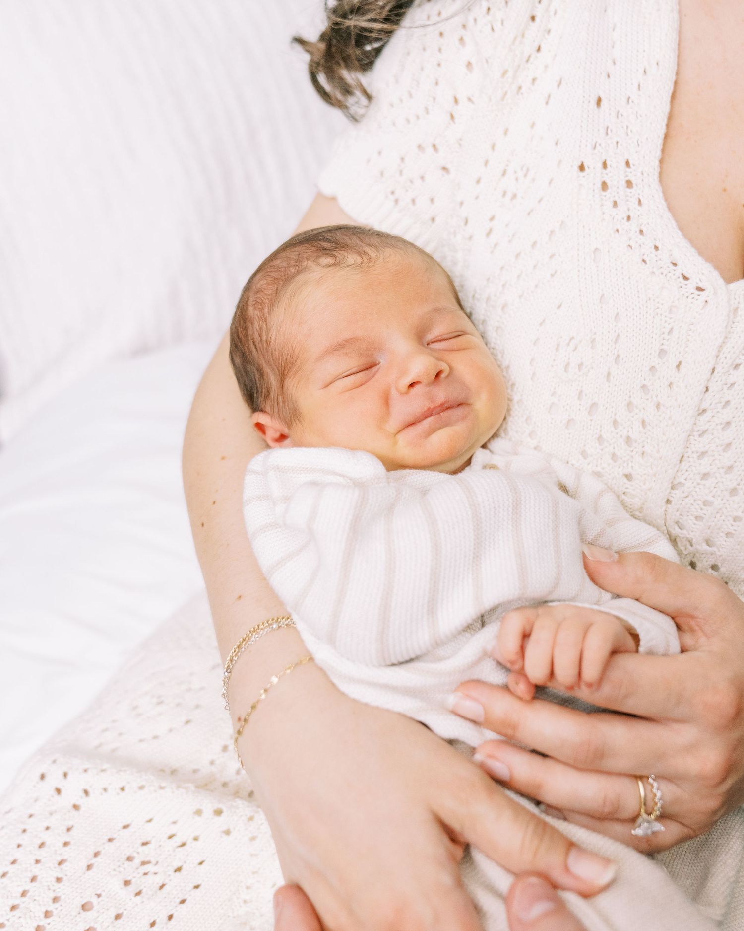 A sleeping newborn baby wearing white clothing rests peacefully on a textured white blanket.