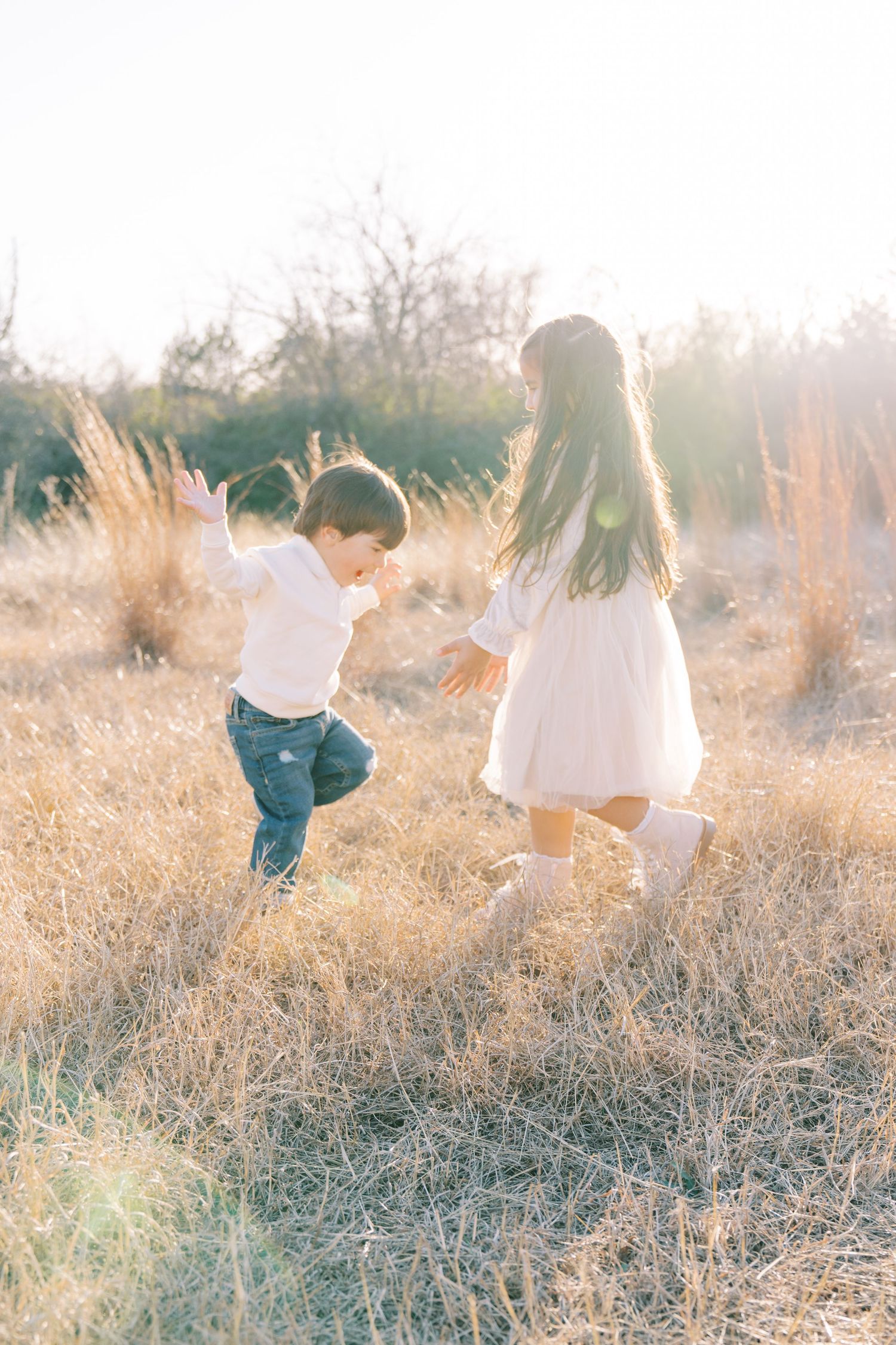 Two children playing joyfully in a sunlit golden field, a boy and girl running together outdoors.