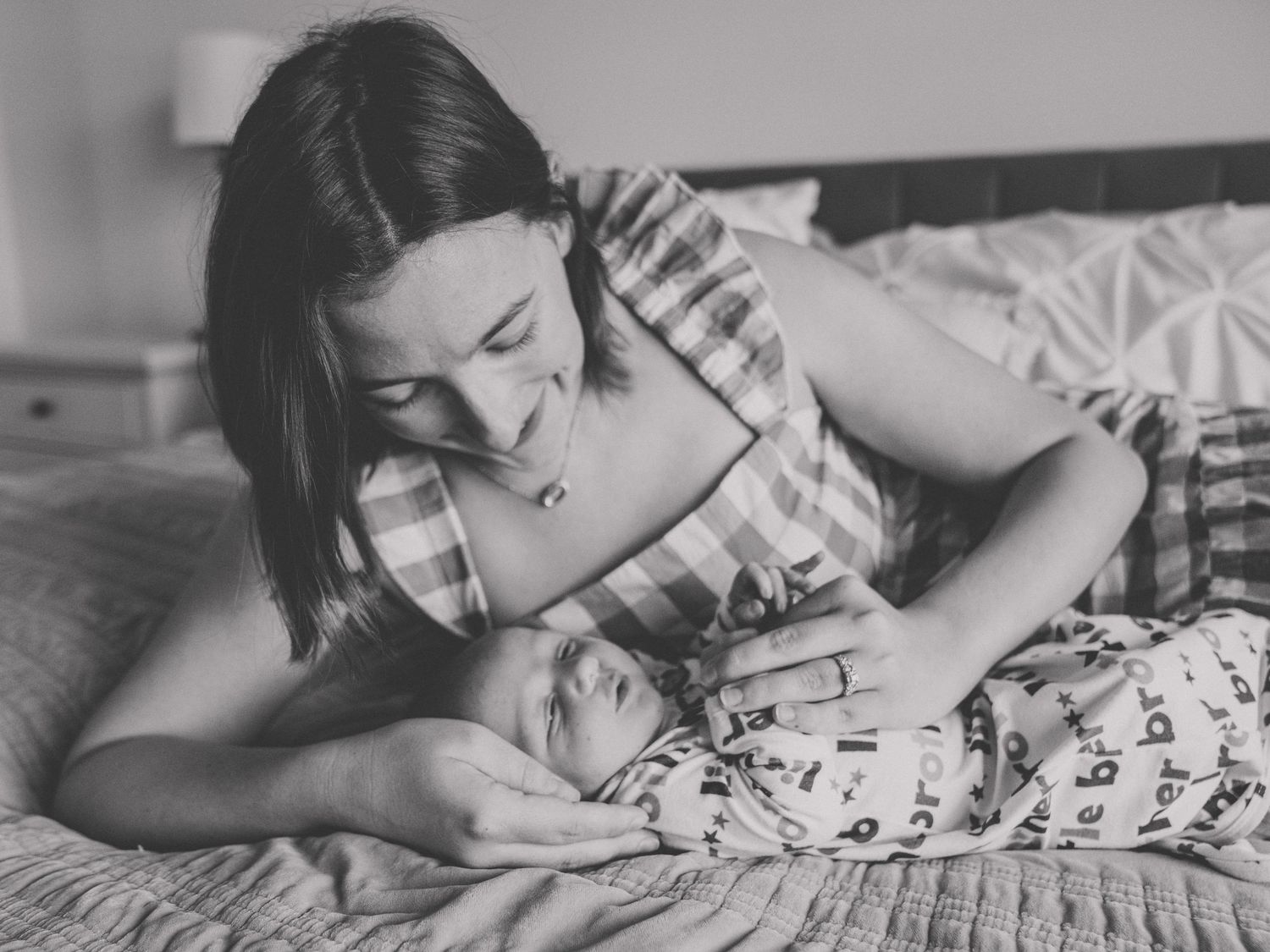 A tender black and white photograph showing a loving parent and child sharing an intimate moment while lying on a bed.