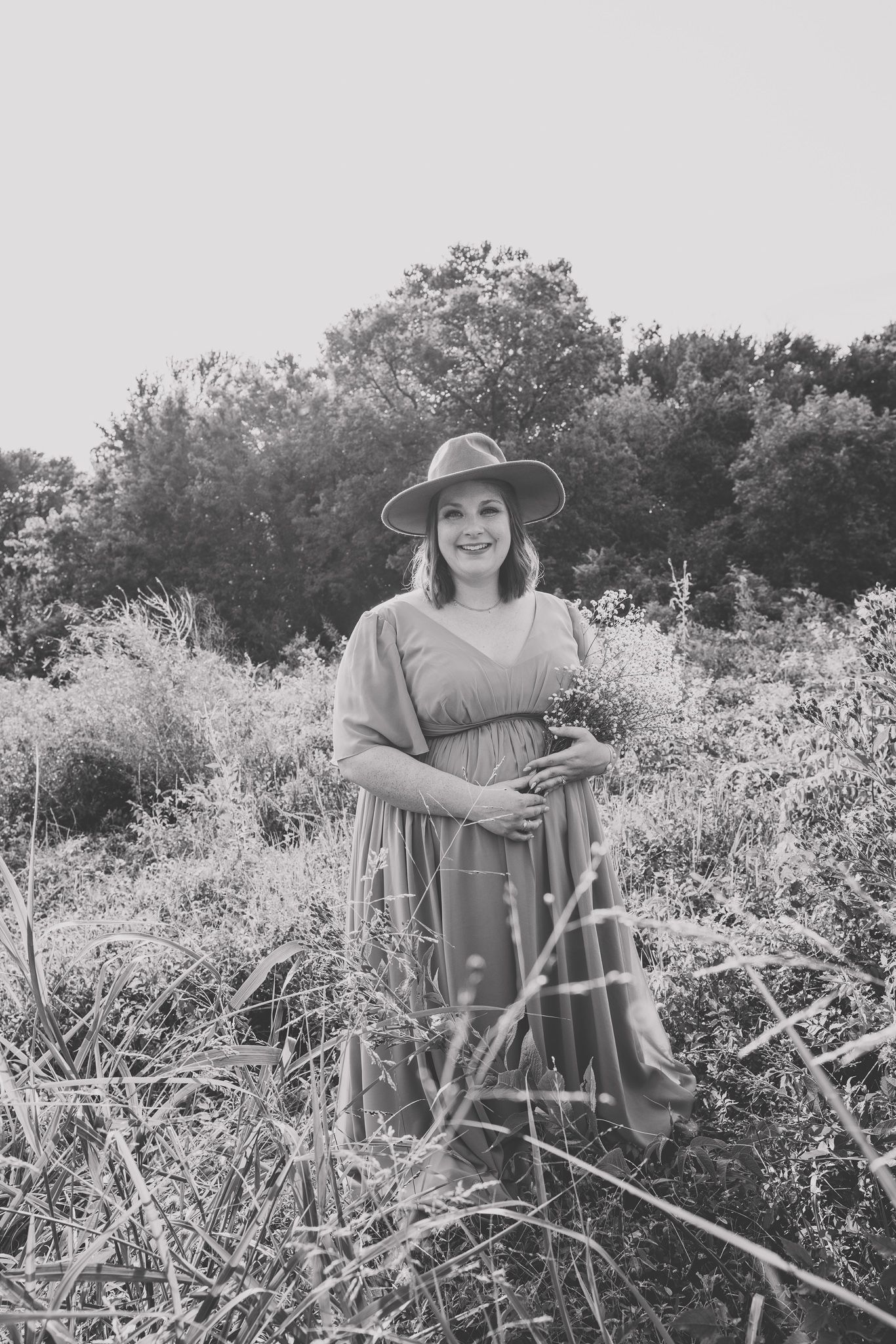 Black and white portrait of someone in a flowing dress posing in a wildflower meadow.