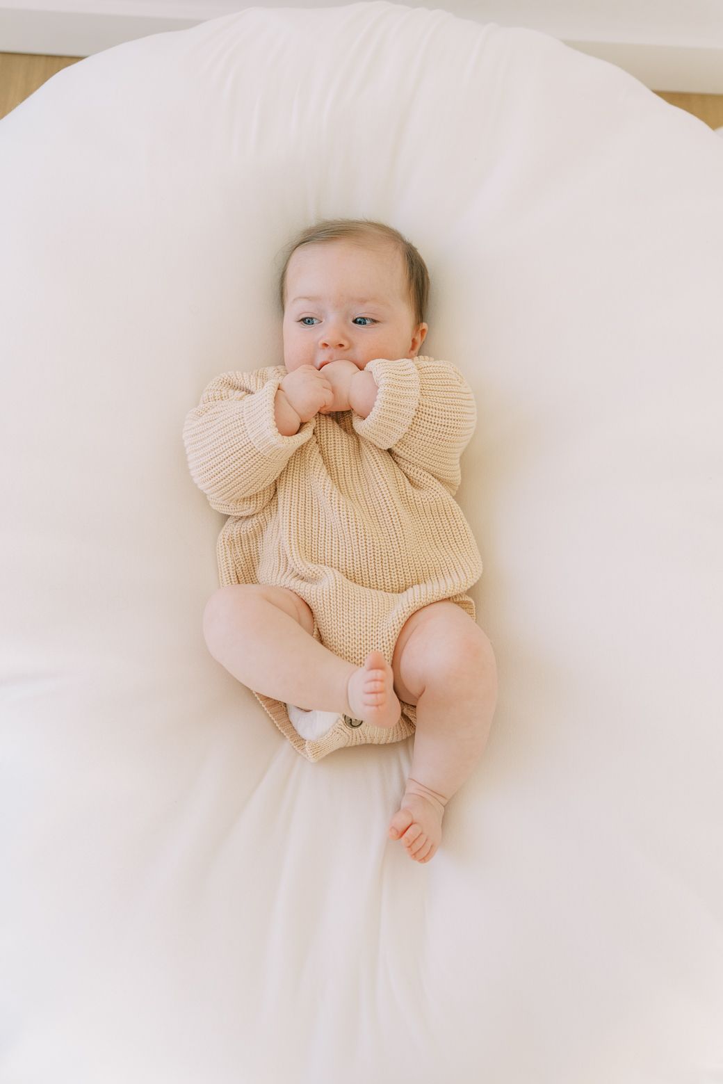 Baby wearing cream colored knit sweater lying on white bedding in various poses.