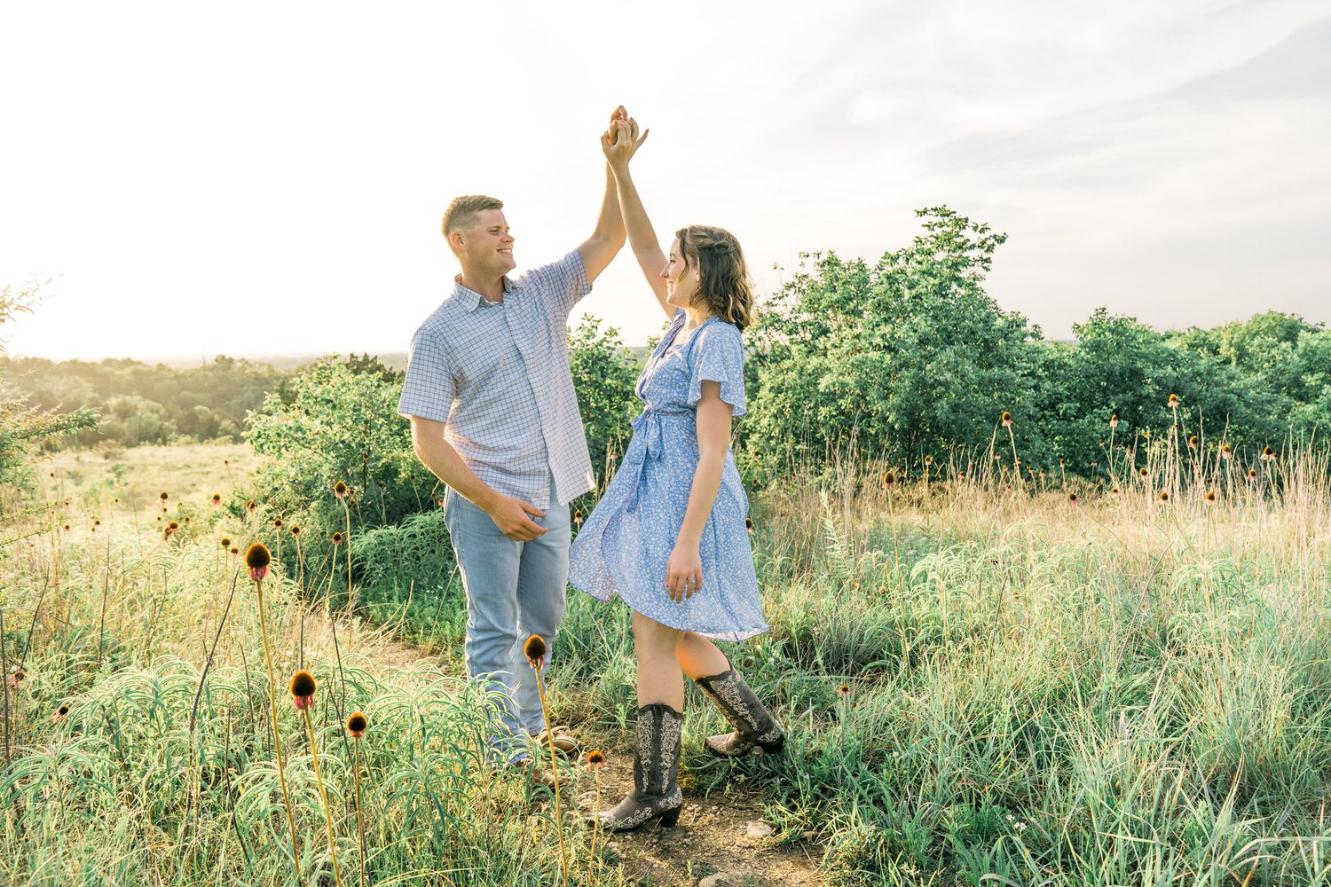 A couple dancing and twirling together in a sunlit meadow with green grass and wildflowers.