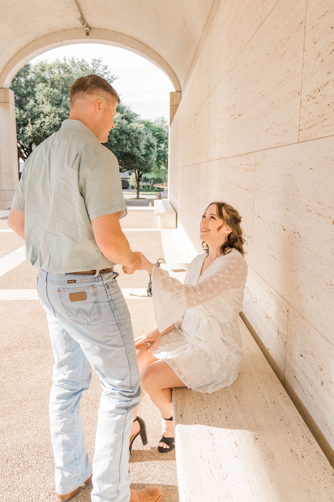 A couple shares a romantic moment under stone archways in a light and airy outdoor setting.