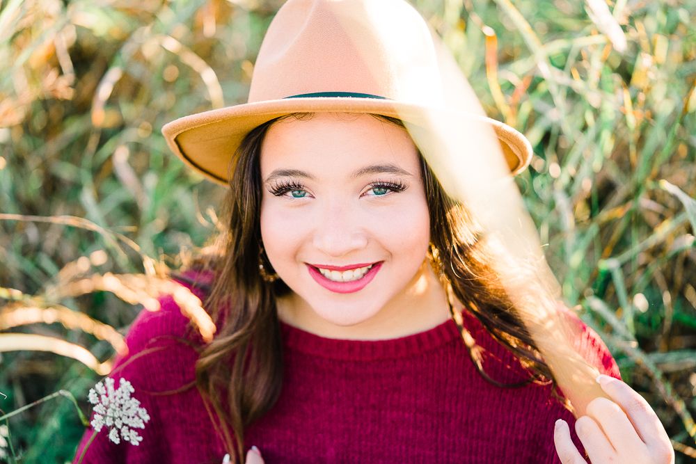 Close up outdoor portrait with burgundy turtleneck and tan hat against blurred green natural background.