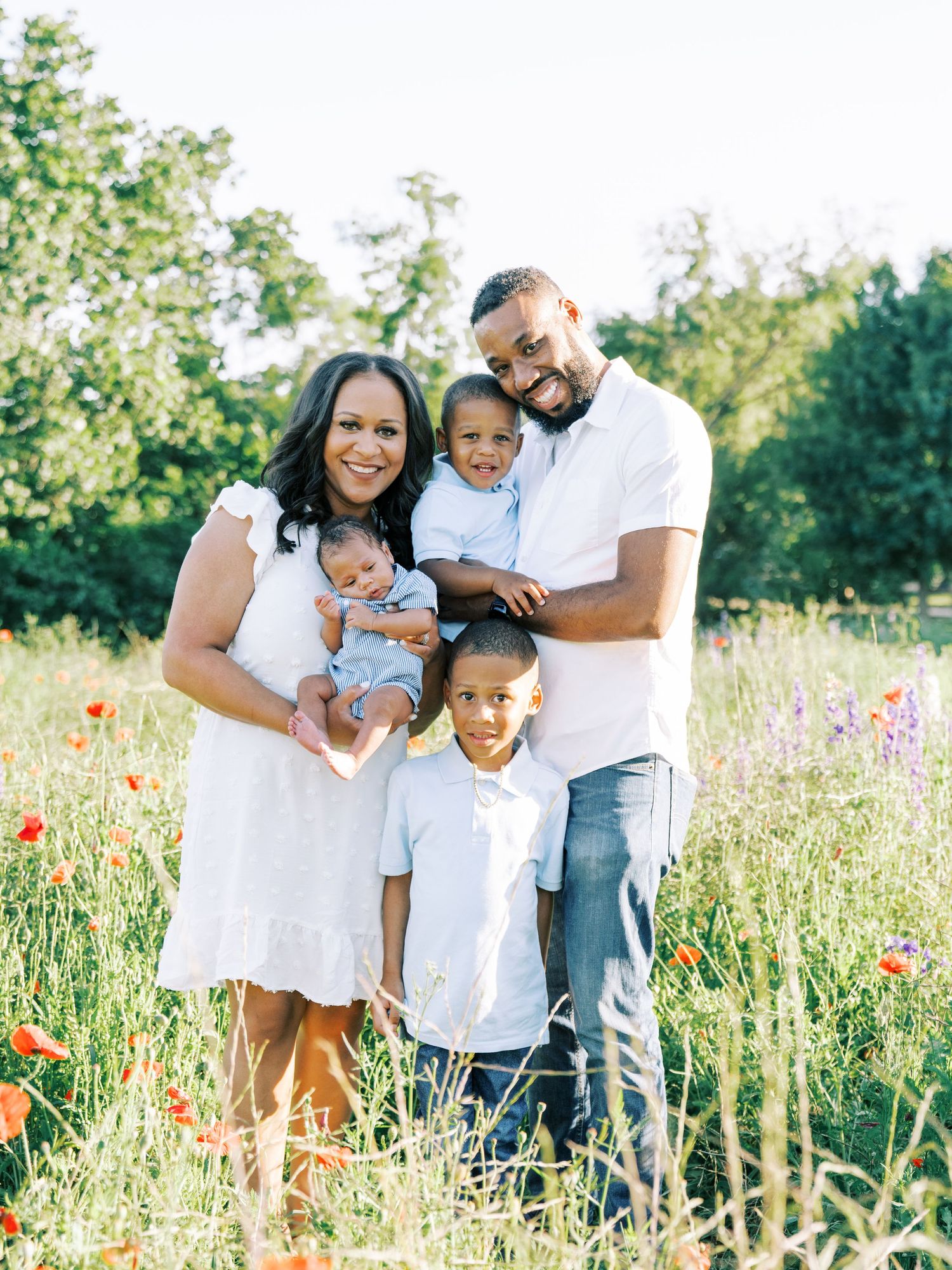 Family wearing white outfits poses together in a wildflower meadow with red poppies on a sunny summer day.