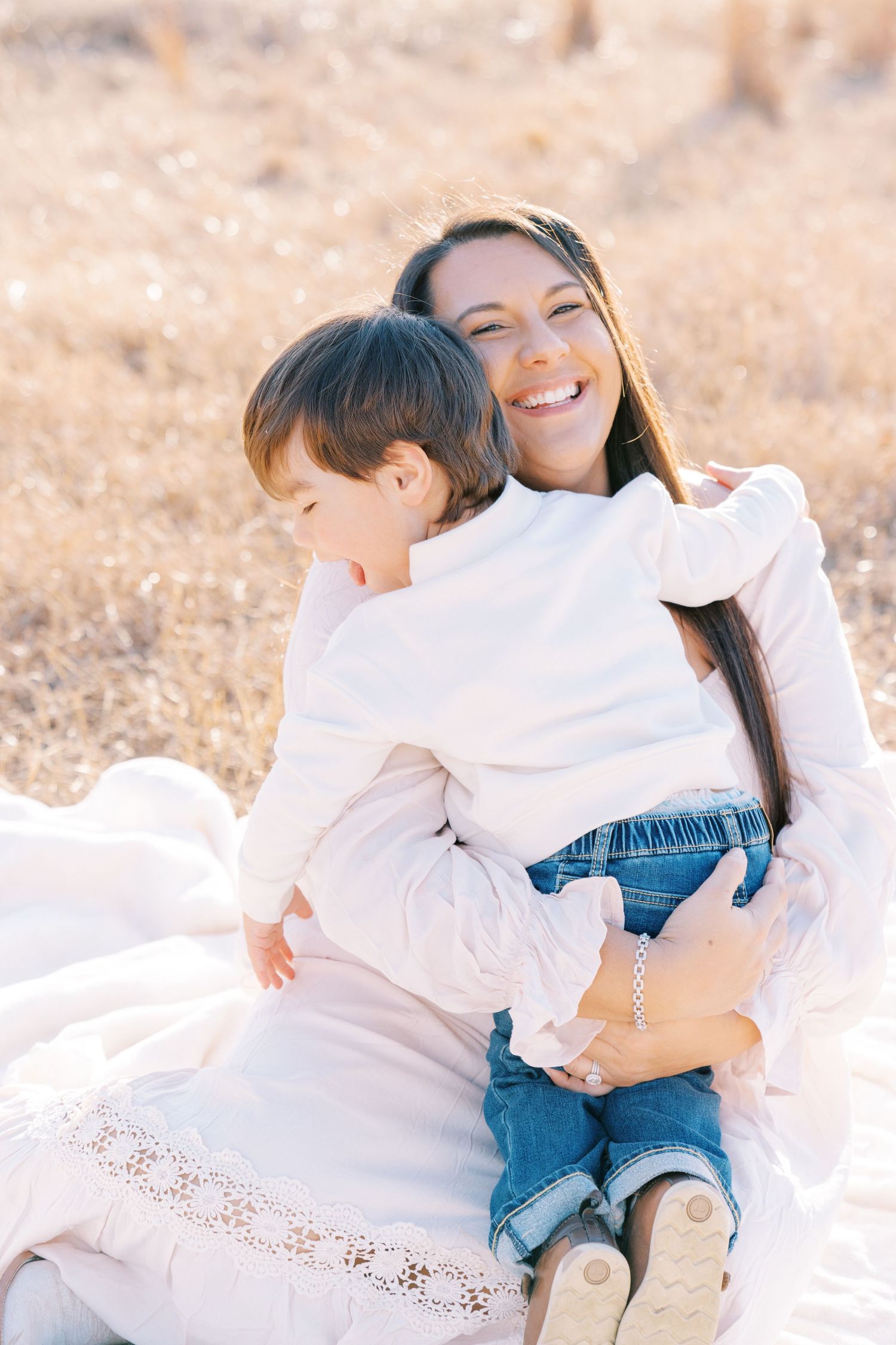 Tender moment between parent and child sitting on white blanket in sunny field.