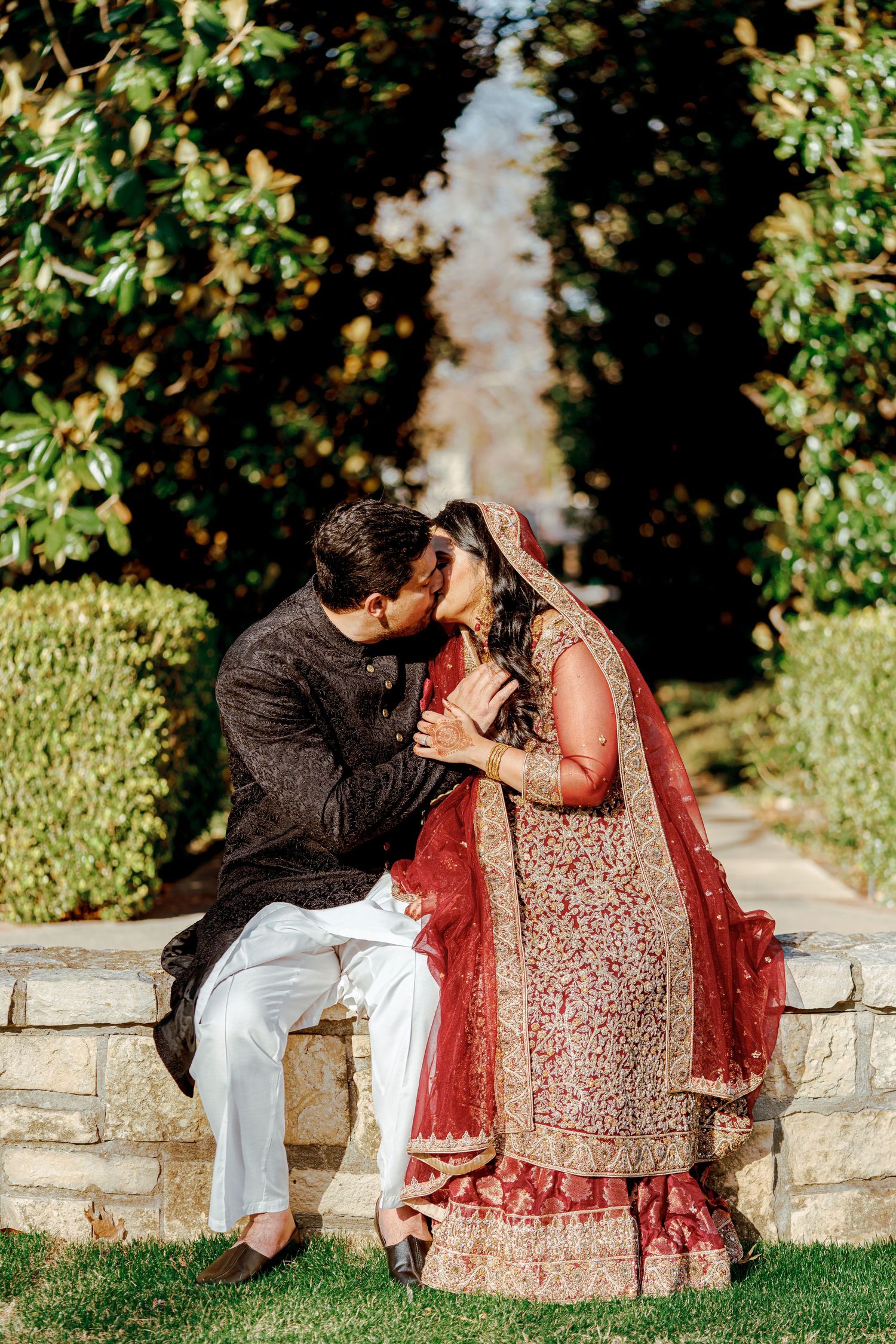 A couple in traditional Indian wedding outfits sharing an intimate moment in a garden setting.