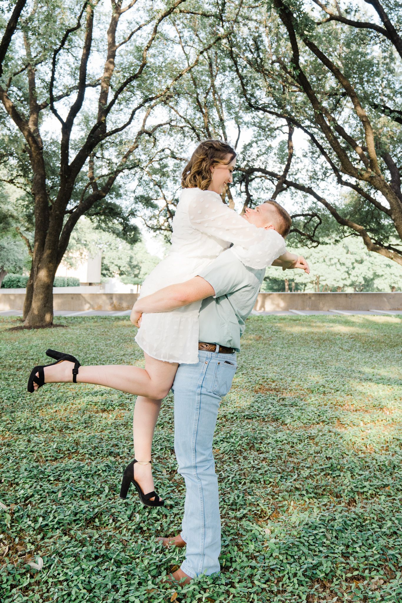Playful couple embraces and dances among olive trees in a romantic outdoor photoshoot.