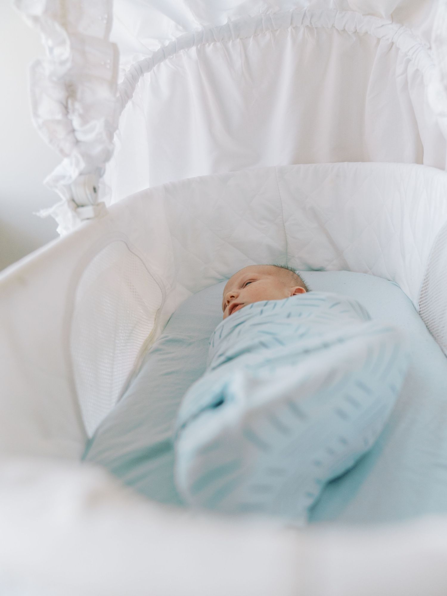 A newborn baby sleeps peacefully in a soft white blanket against white bedding.