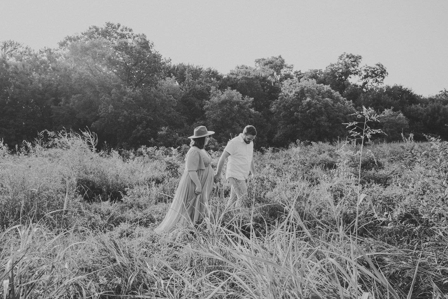 A black and white photo of people walking through tall grass in a natural outdoor setting.