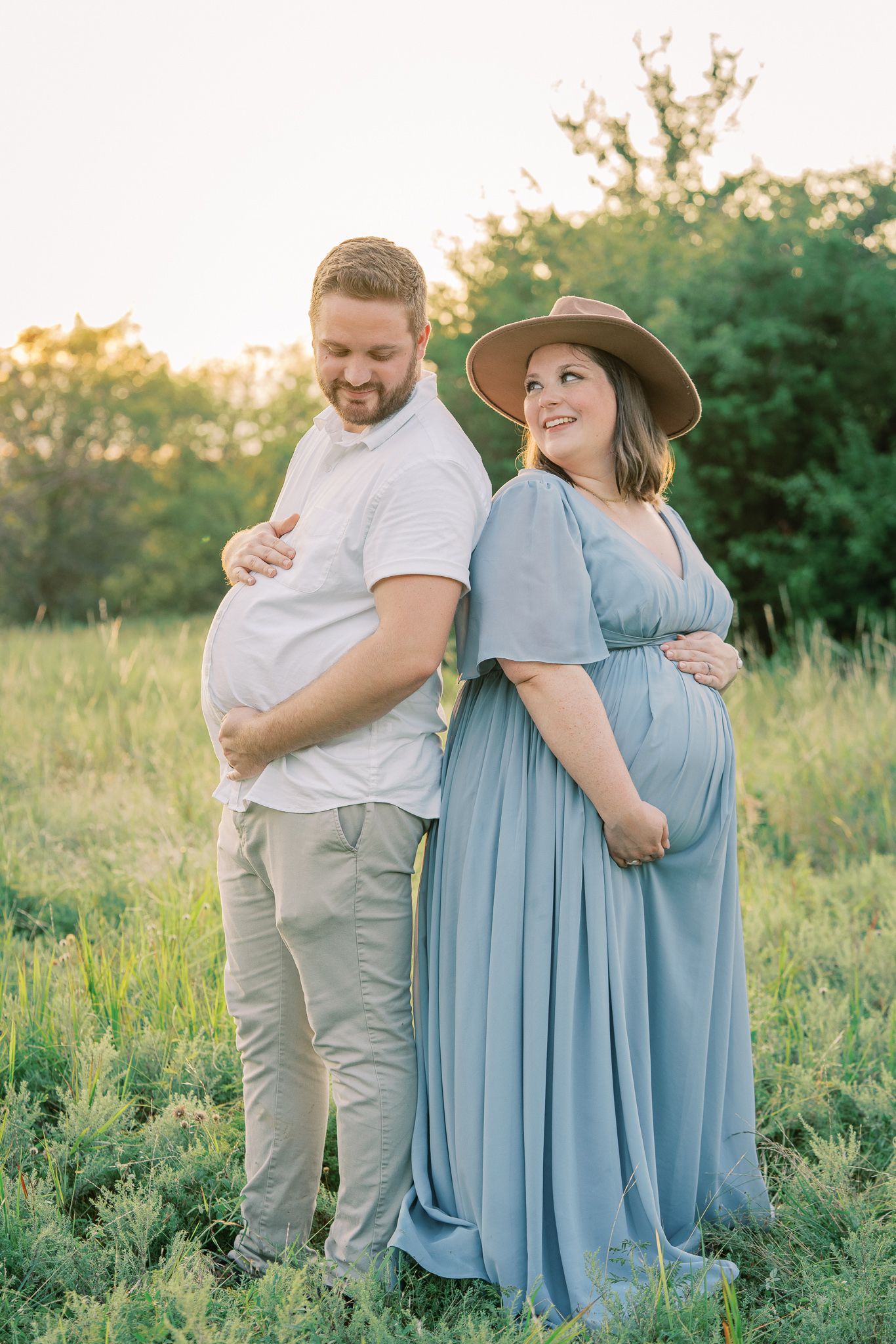 A couple and two people in light blue dresses embrace in a sunlit meadow during a summer photoshoot.