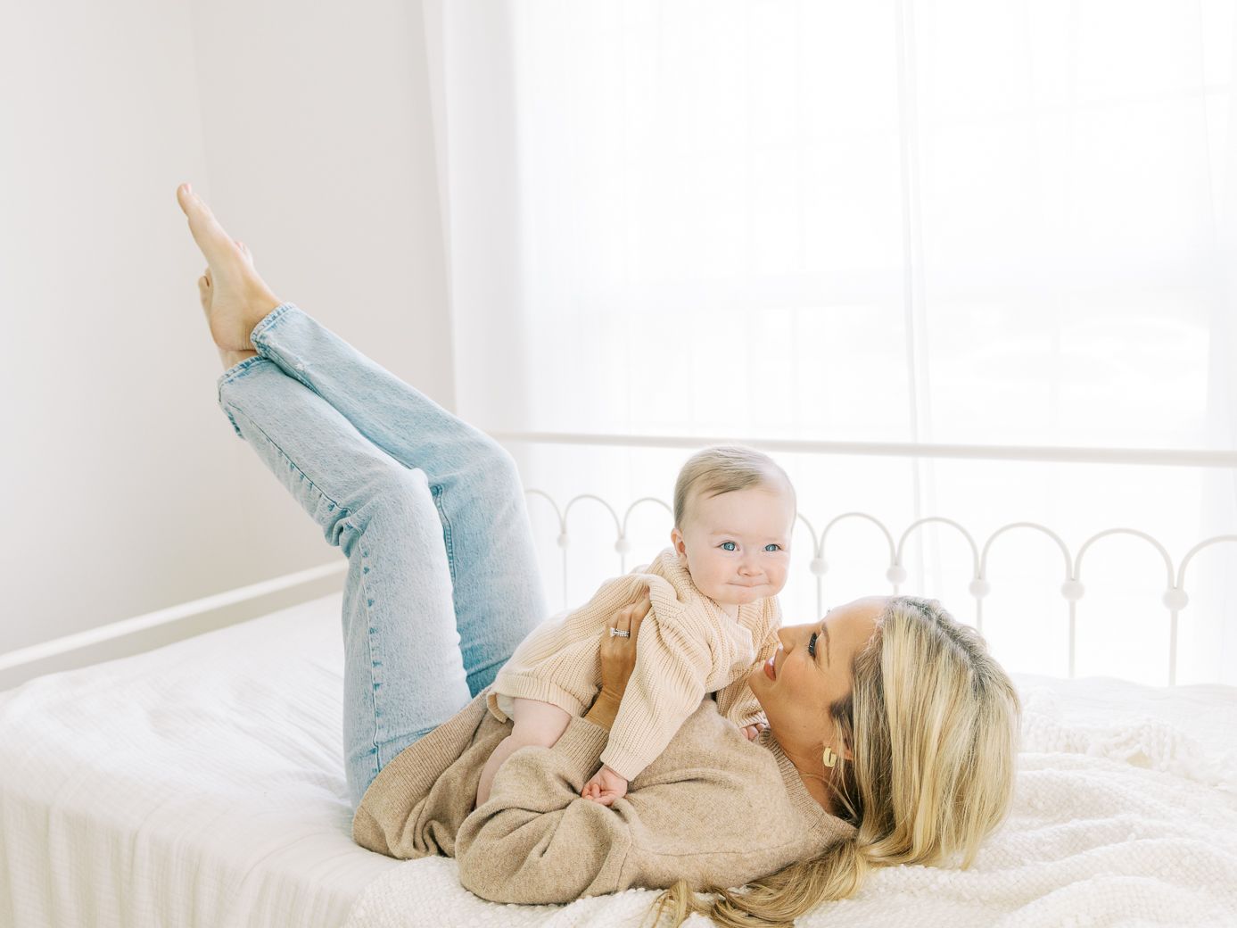 Mother and child lounging on white bedding while playing and bonding together in a bright bedroom.