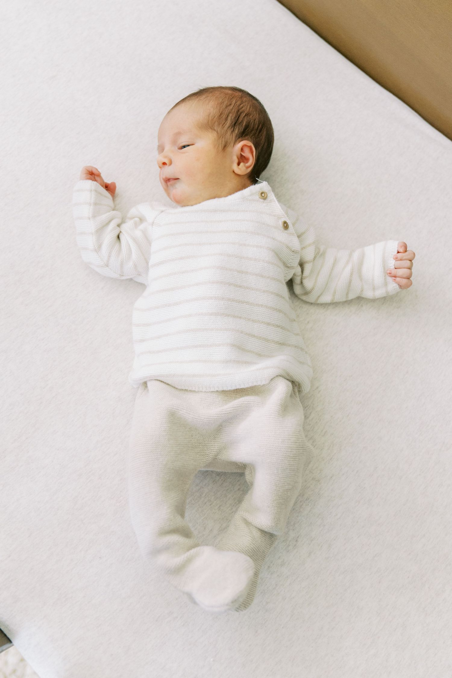 A sleeping baby in white clothing lies peacefully on white bedding in a series of connected photos.