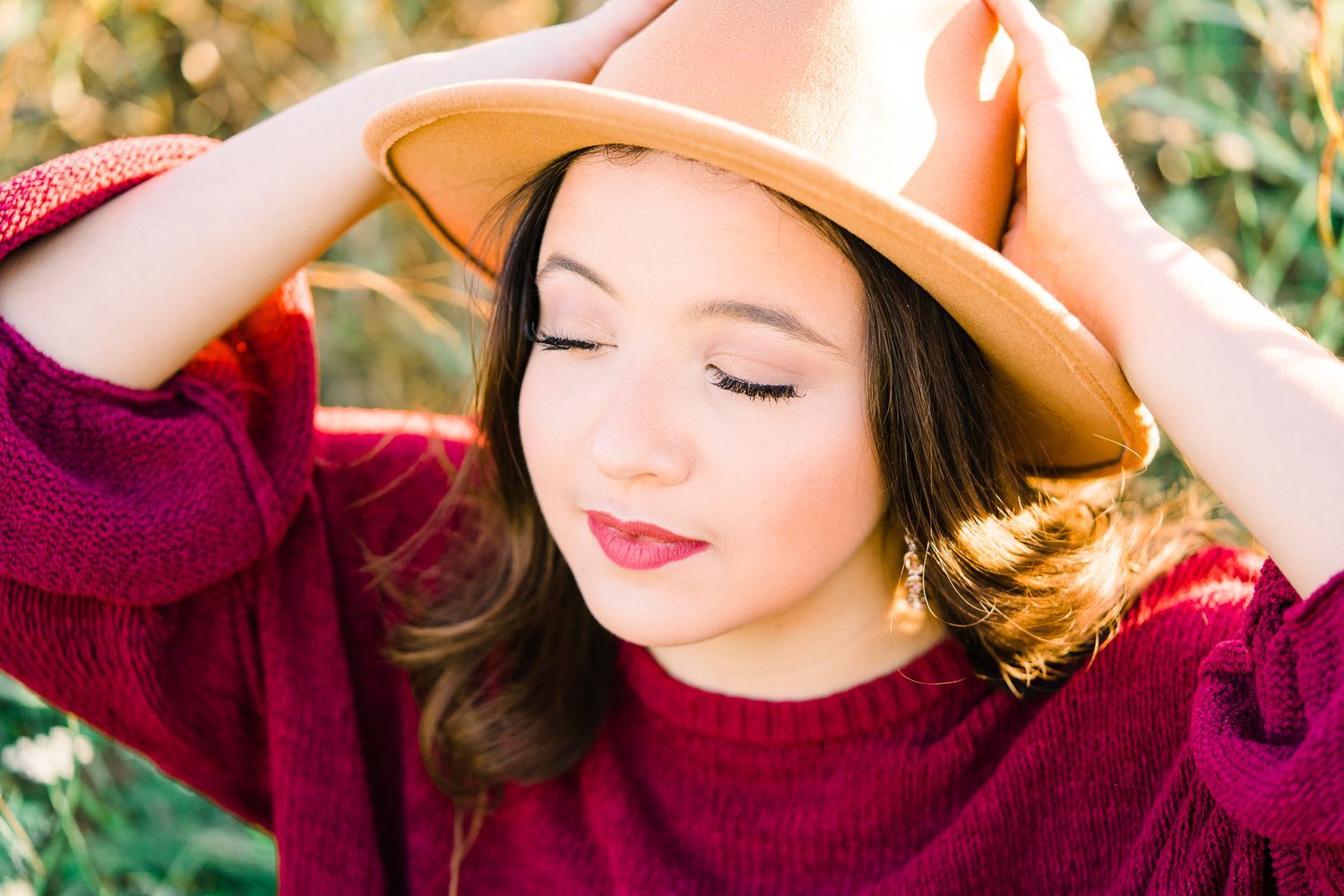 Close-up outdoor portraits with warm lighting showing different expressions while wearing a tan hat and burgundy sweater.