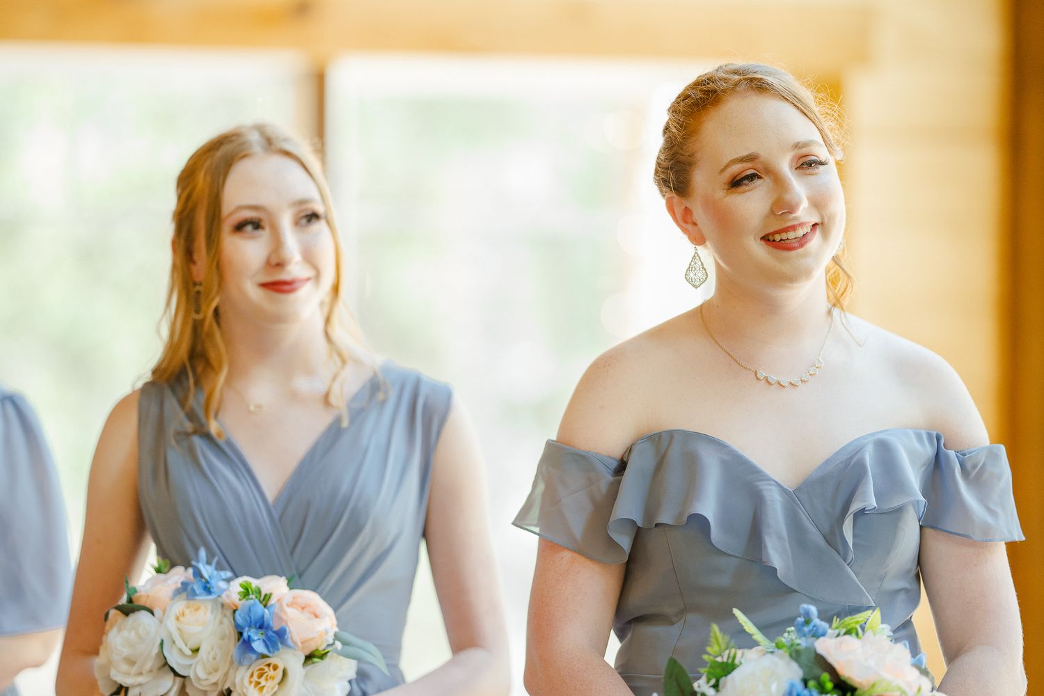 Bridesmaids in light blue dresses stand together holding white and blue floral bouquets at an indoor venue.