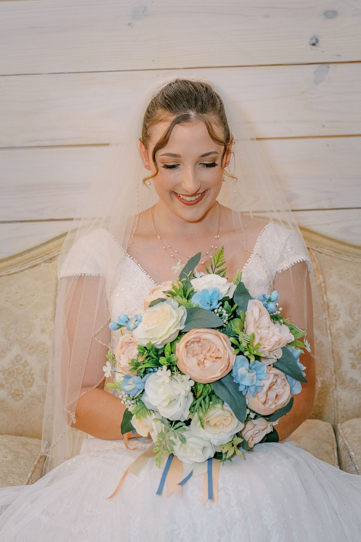 A bridal bouquet featuring soft peach roses, white peonies, and light blue hydrangeas against a white dress.