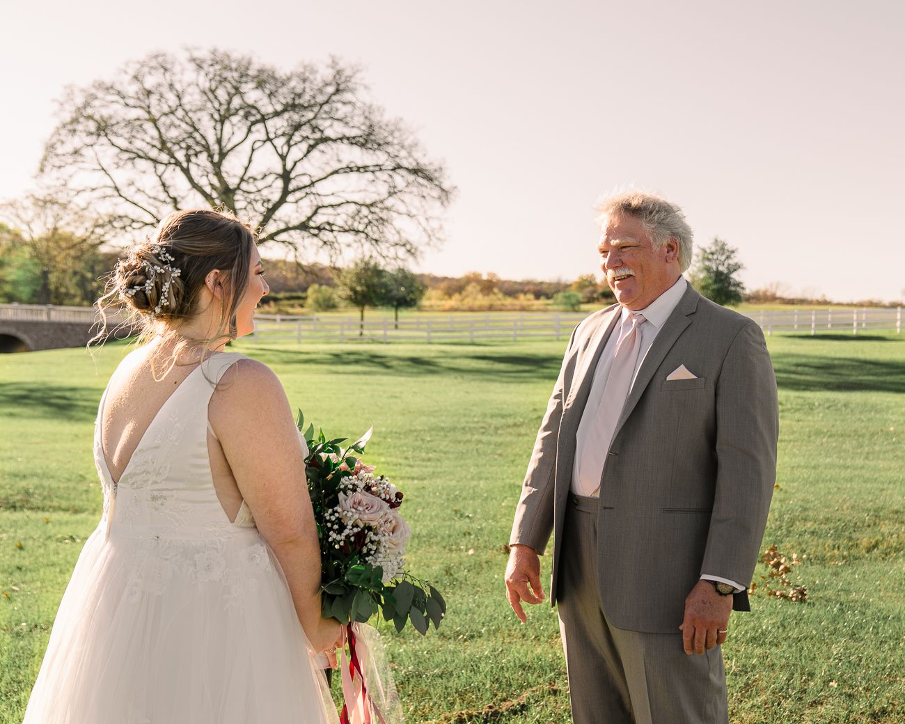 A tender moment between two people in formal attire standing on a grassy field during golden hour.