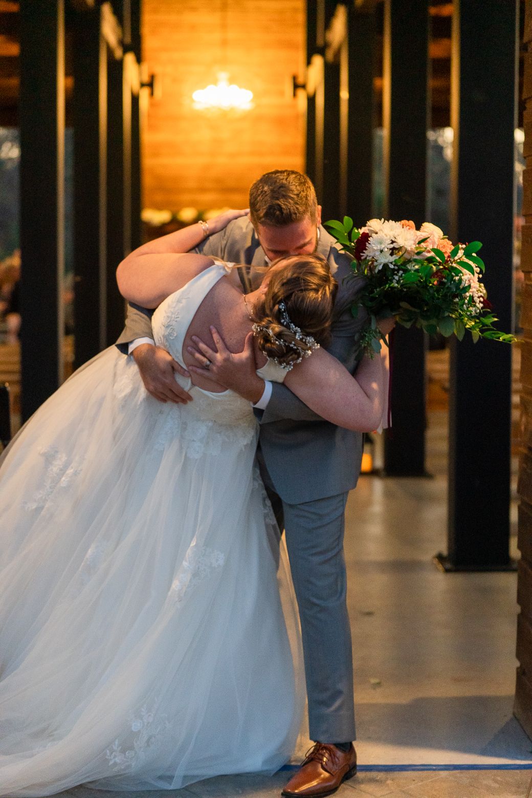 A romantic dip kiss sequence between newlyweds at their wedding, with the bride in a flowing white gown and groom in gray.