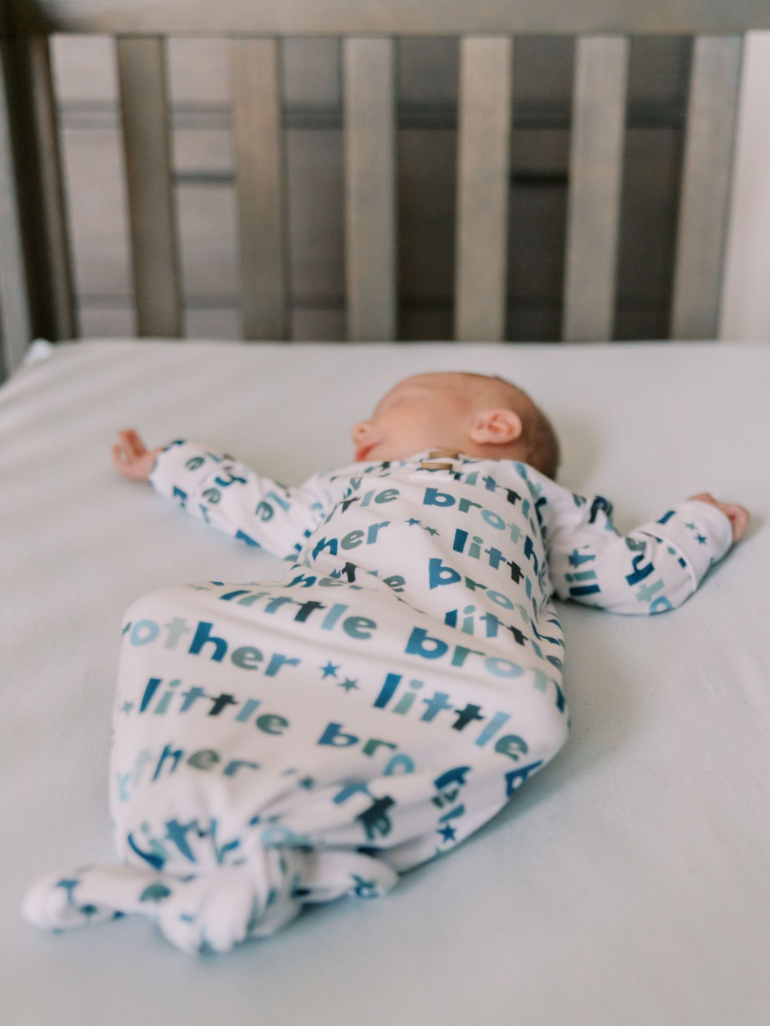 Sleeping baby in patterned swaddle blanket lies in white crib.