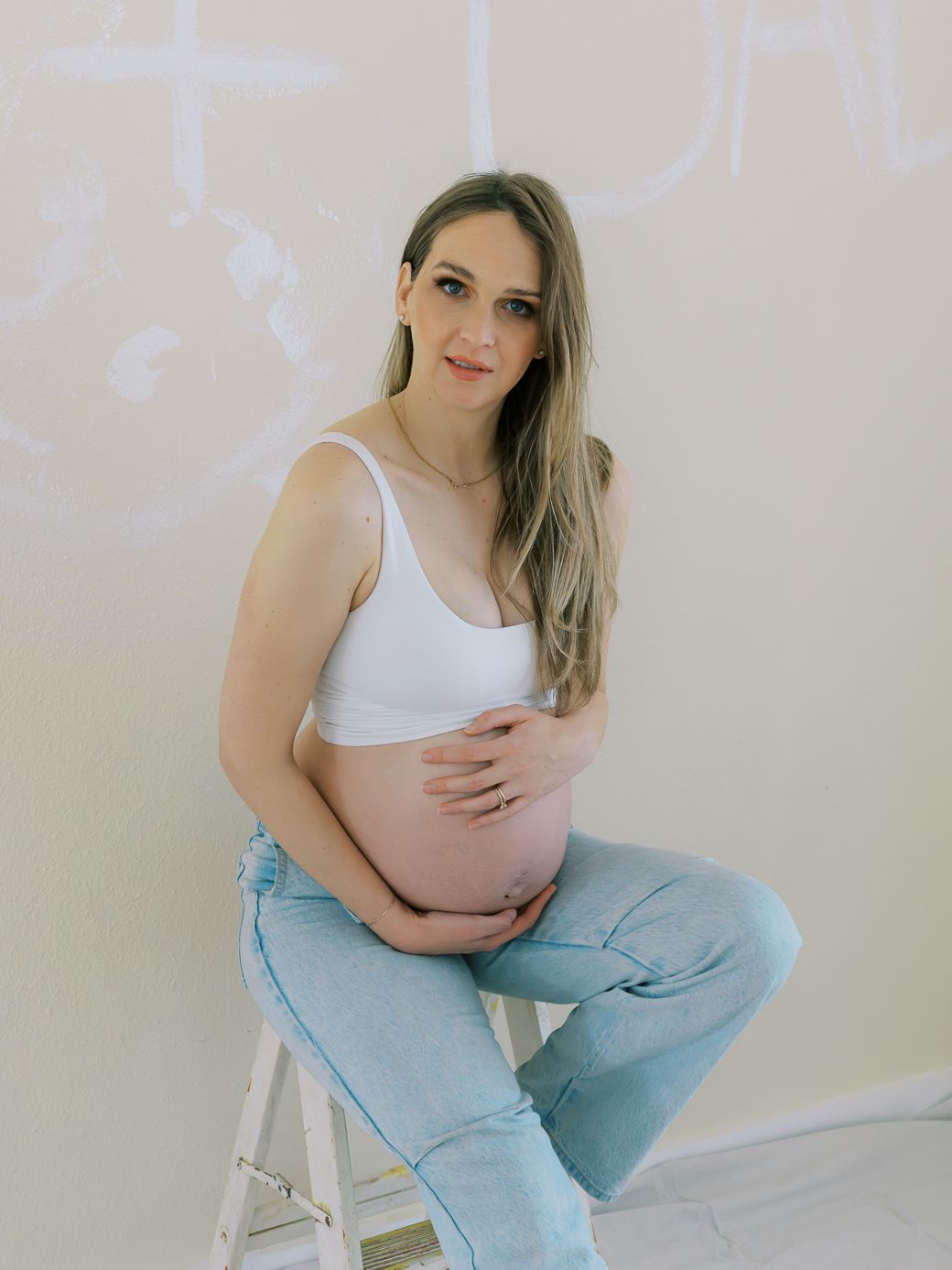 A maternity portrait featuring light wash denim and white tank top in a bright room.