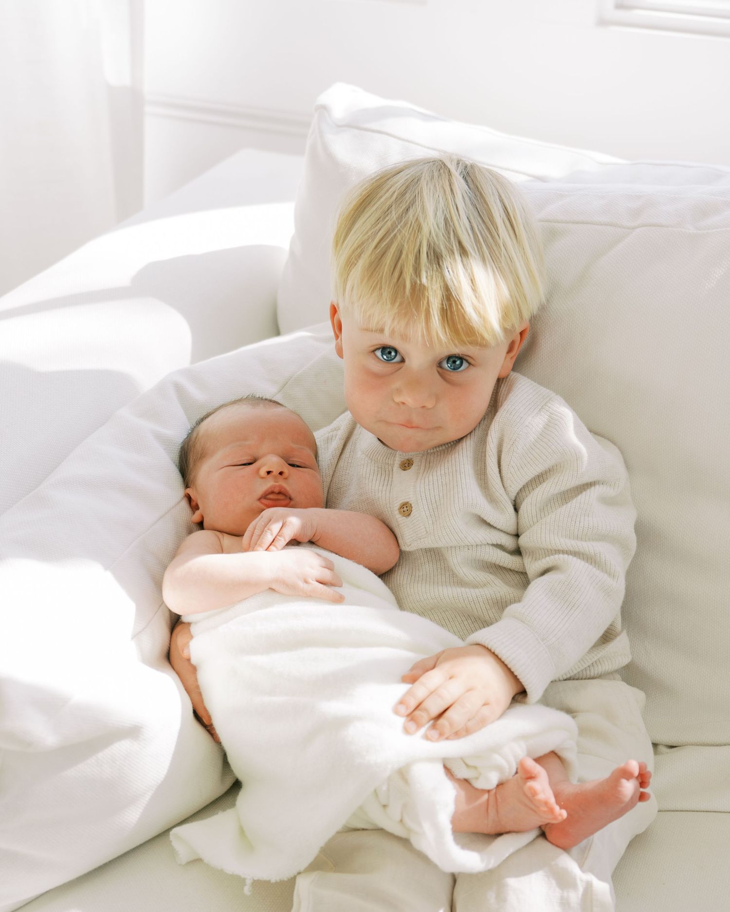 Two children in white clothing snuggling together on white bedding.