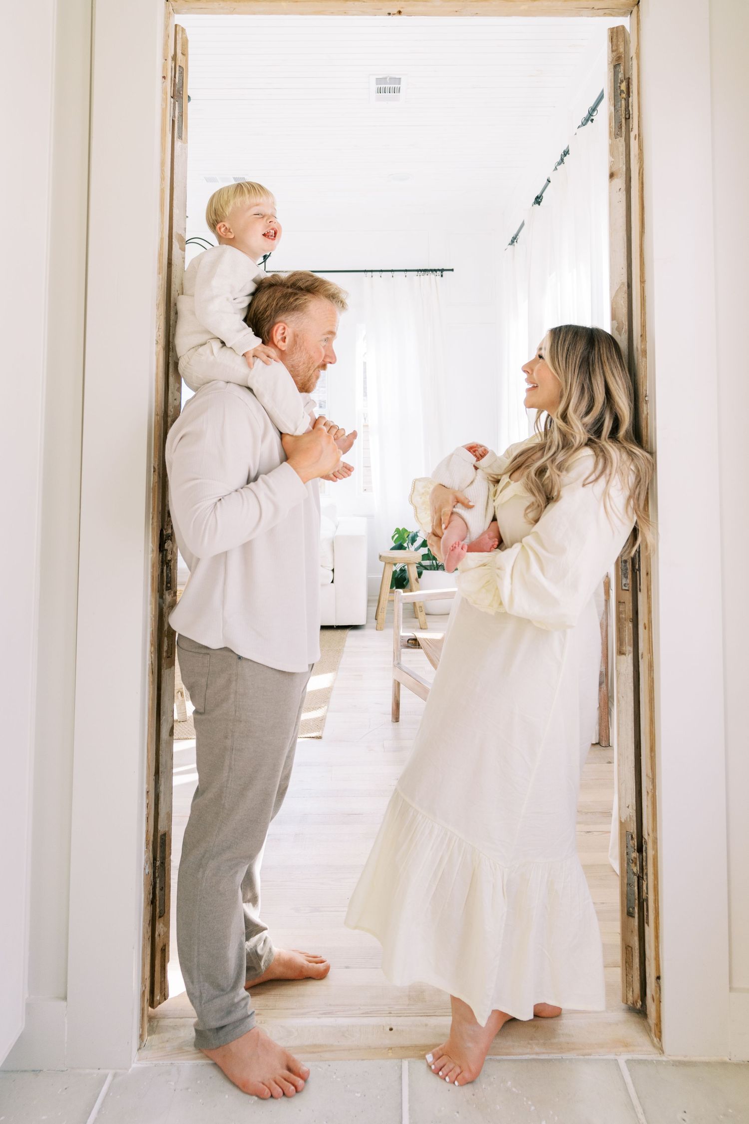 A family in white and neutral clothing shares a joyful moment together in a bright doorway of their home.