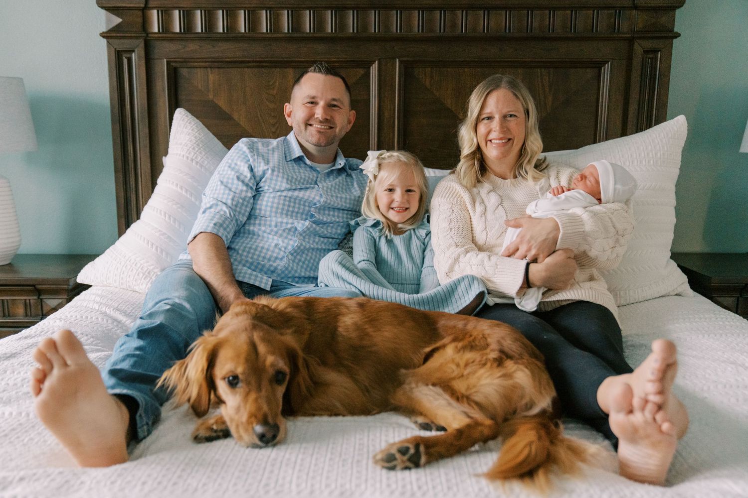 Family lounging together on bed with their golden retriever dog in candid home photos.
