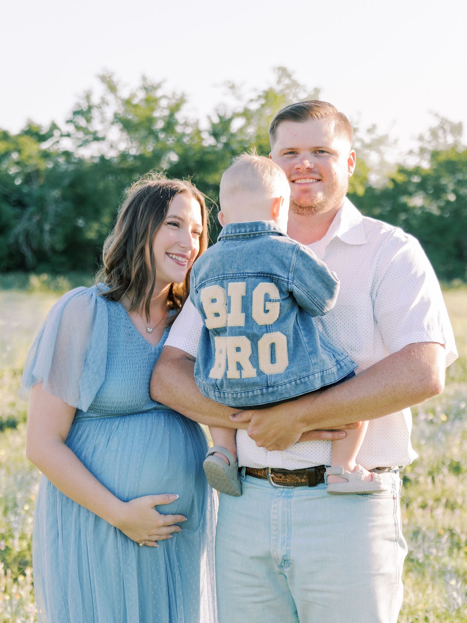 Couple in matching denim and white outfits embrace lovingly in a sunlit field during golden hour.