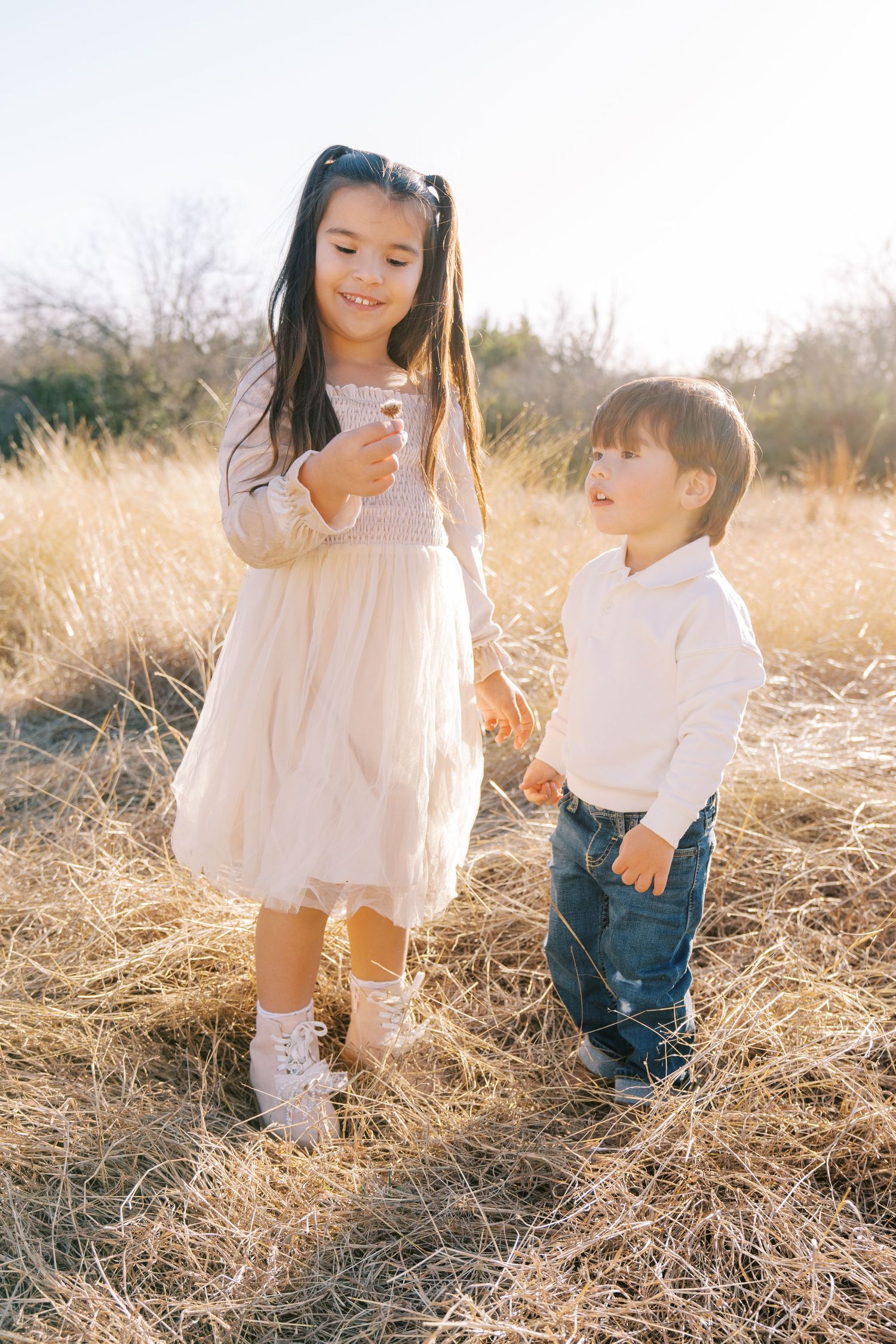 Children play together in a golden field of tall grass during sunset, creating a whimsical outdoor scene.