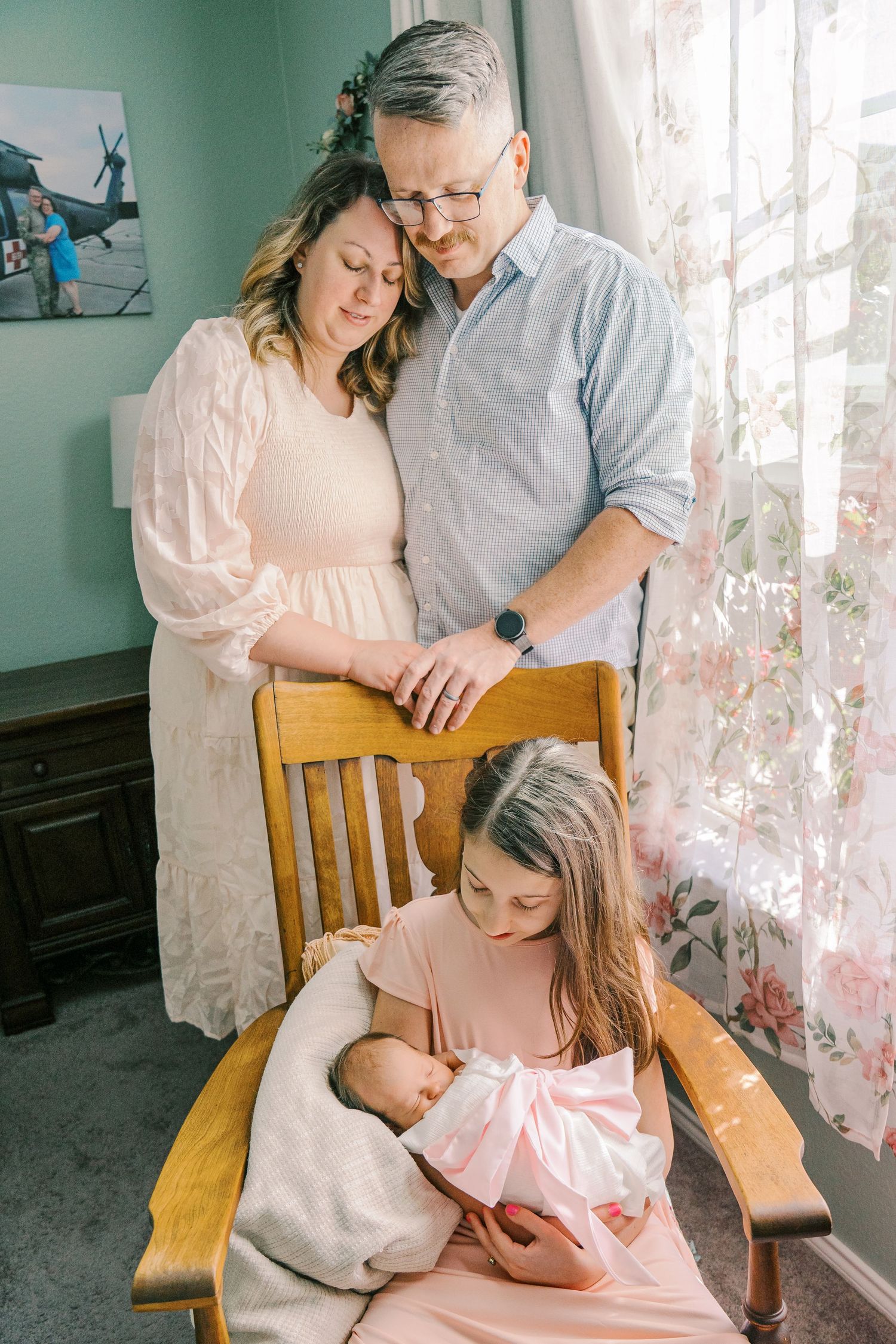 Family gathered on wooden chair by window with soft natural lighting and mint green walls.