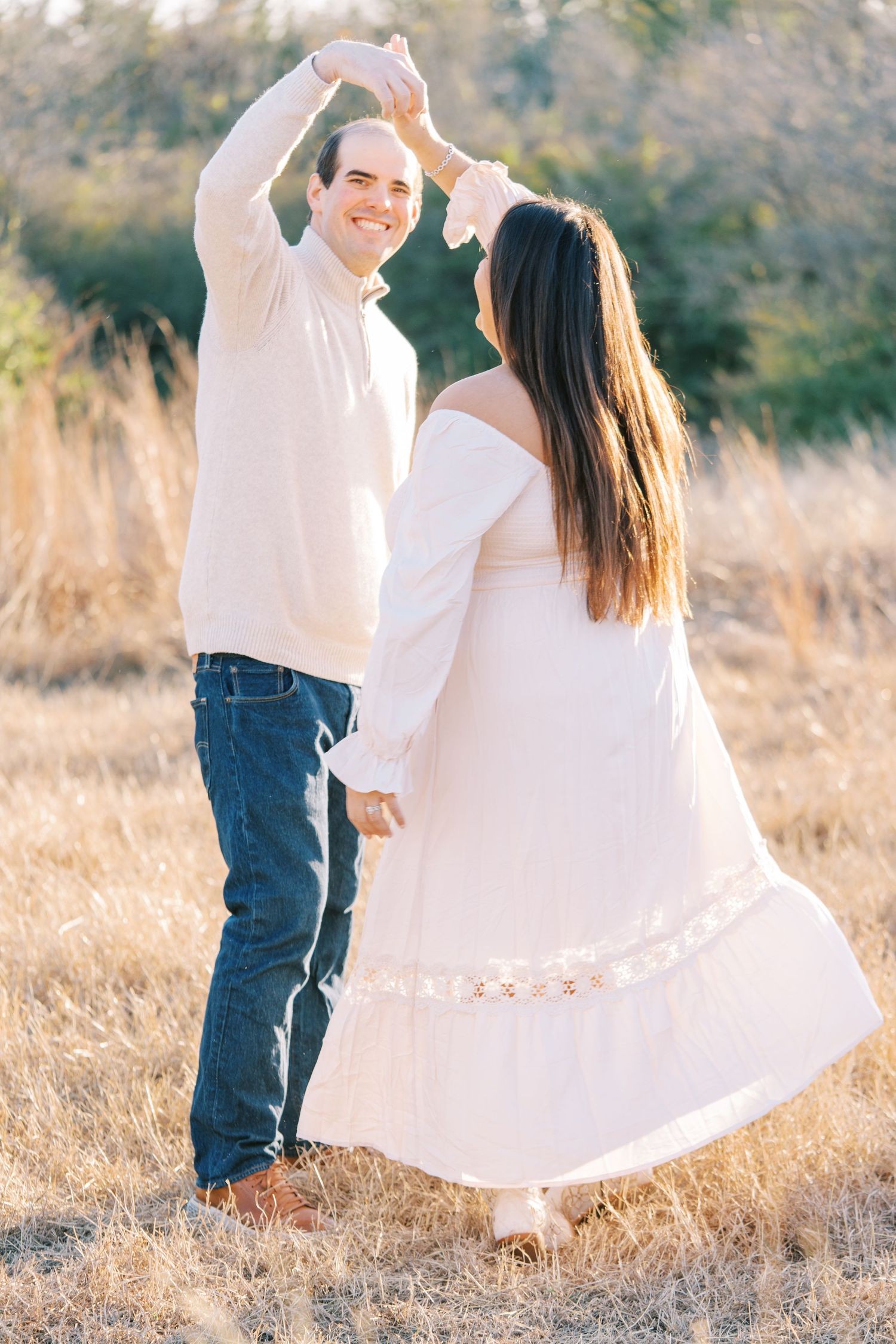 Couple dancing in golden field, man in white shirt and jeans twirling woman in flowing white off-shoulder dress.